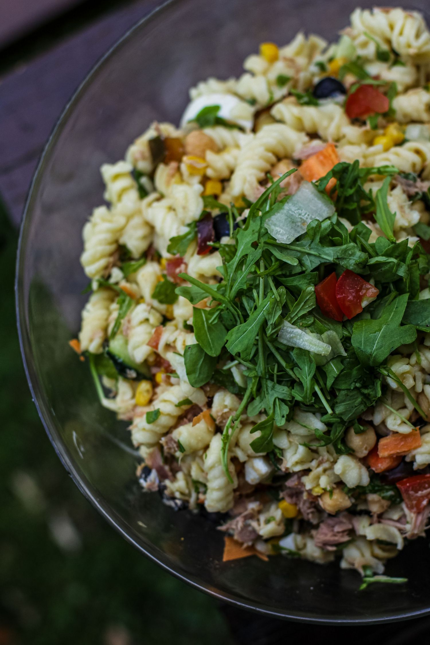 Fresh pasta salad with colorful vegetables and herbs served in a glass bowl.