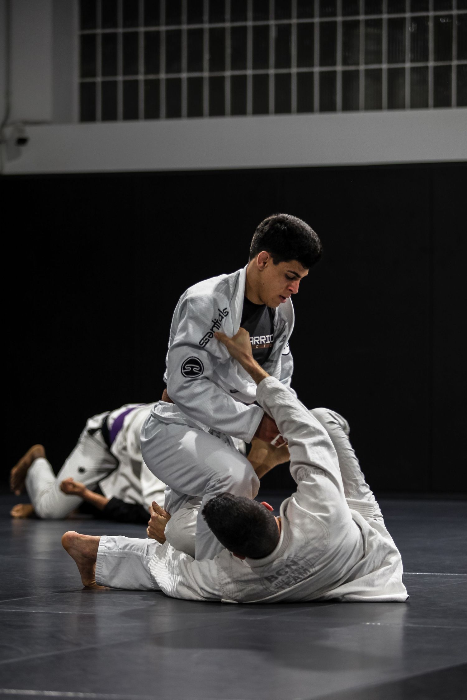 Martial artist practicing ground movements in white gi on dark training mat.