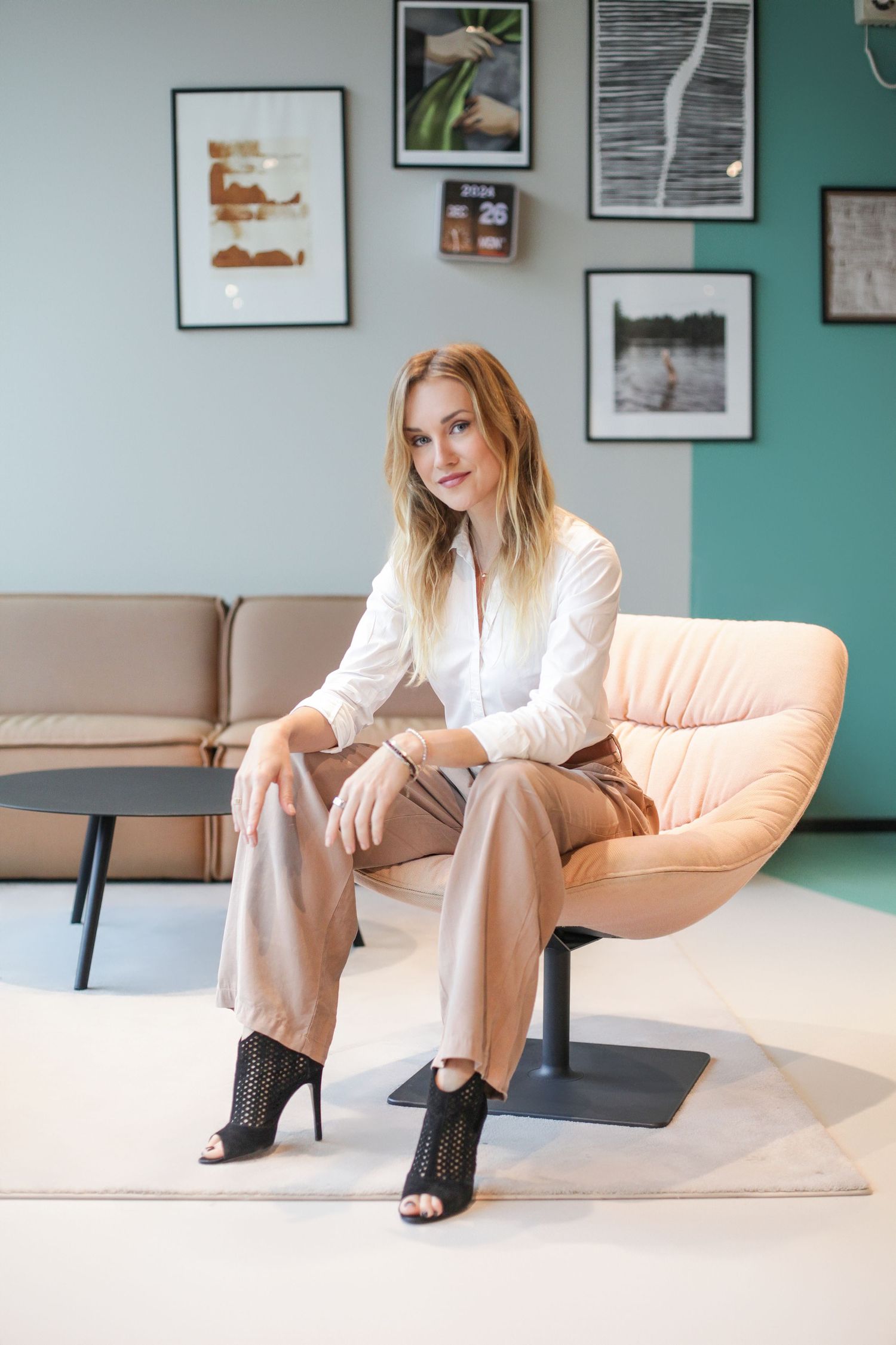 Stylish business portrait in beige outfit sitting on modern furniture with framed art wall.