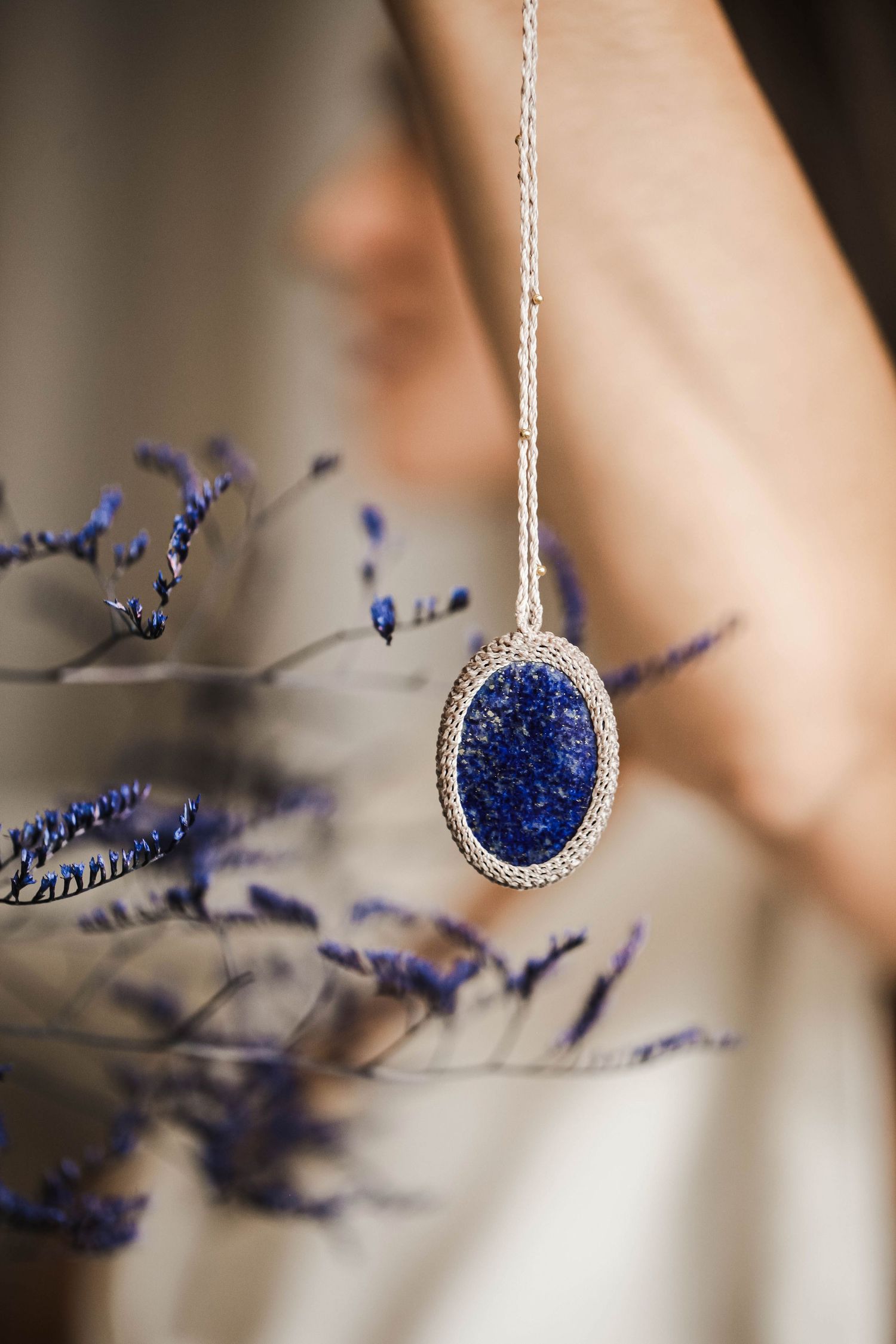 Elegant blue crystal pendant necklace photographed with lavender flowers in soft focus.