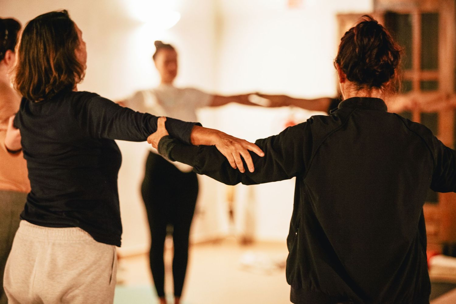 Silhouettes of people dancing with arms raised in a warm-lit room.
