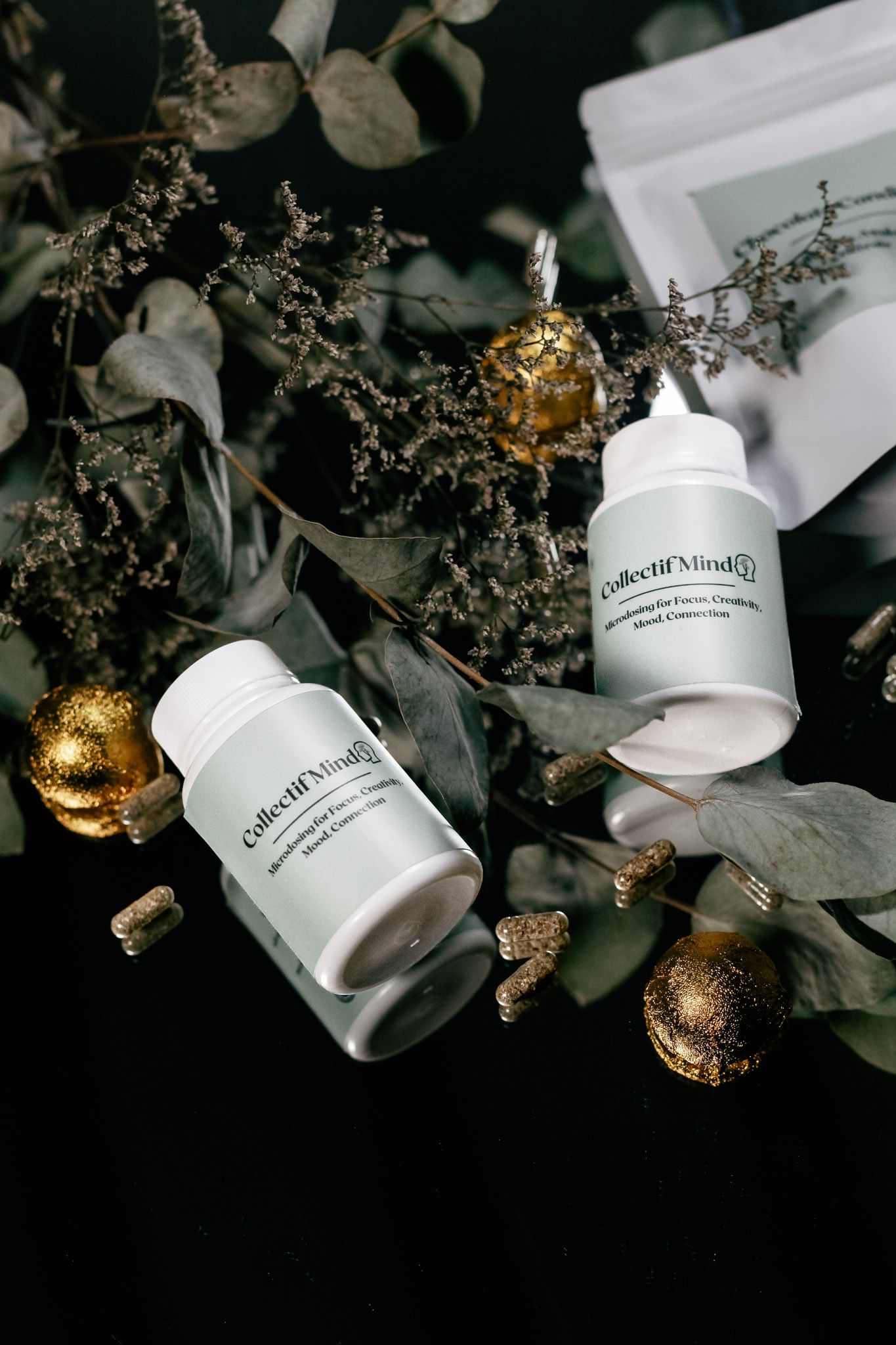 White cosmetic product bottles arranged with gold ornaments and dried flowers on dark background.