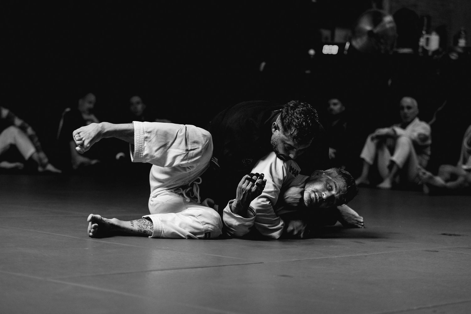 Two athletes engaged in ground combat during a martial arts competition on a dark mat.