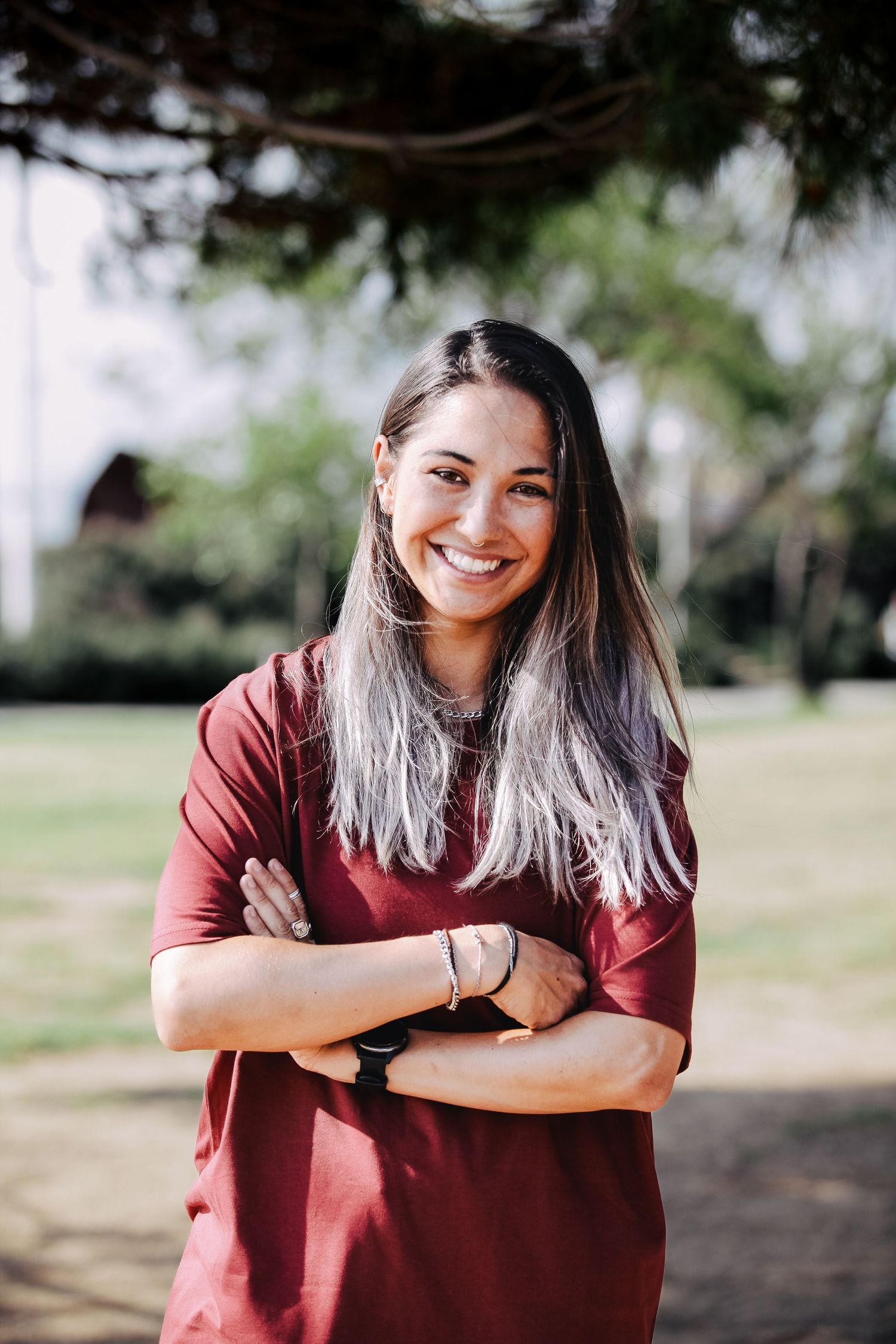 Person in burgundy t-shirt laughing while posing outdoors in a park setting.