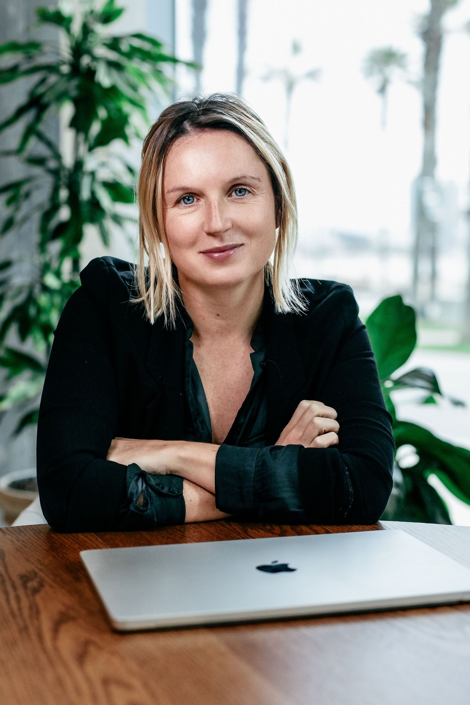 Business professional poses with laptop in modern office with indoor plants.