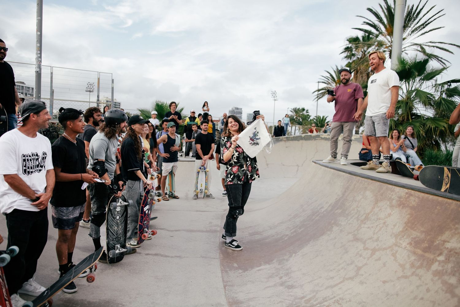 Skateboarders gathered around a skate ramp watching someone perform tricks at an outdoor skate park.