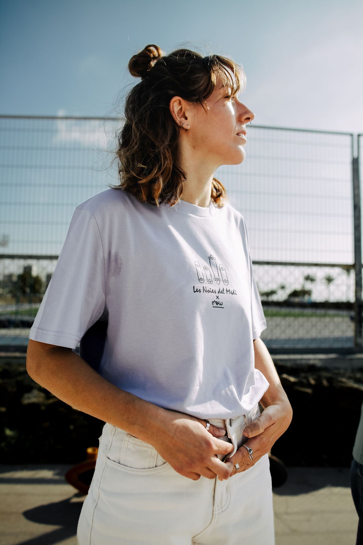 Casual summer style featuring white graphic tee and messy bun in bright sunlight.