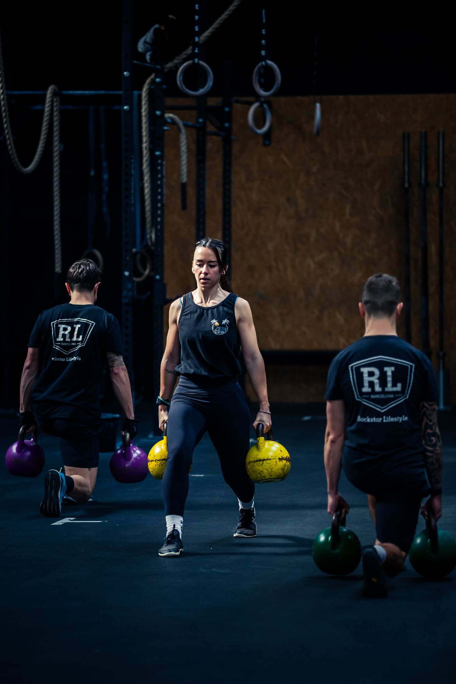 Three people training with kettlebells in a dark CrossFit gym setting.