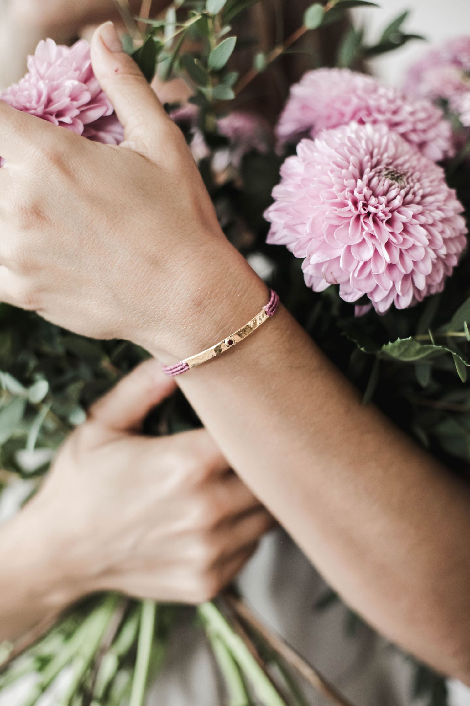 Delicate rose gold bracelet shown against pink flowers and greenery in a feminine composition.