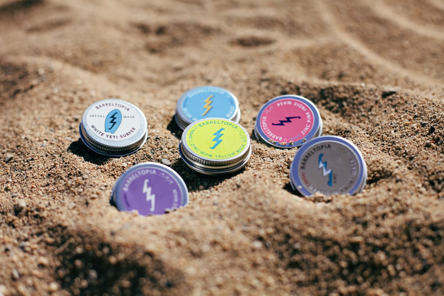 Colorful lightning bolt enamel pins arranged in sand creating playful beach scene.