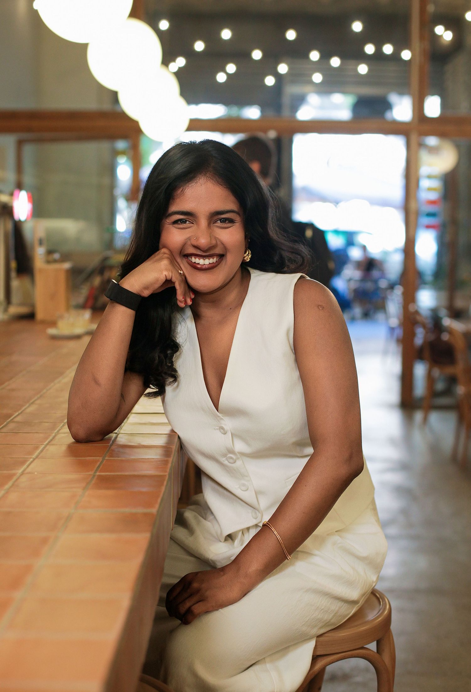 Candid portrait in white sleeveless dress sitting on terracotta tiles with ambient lighting.