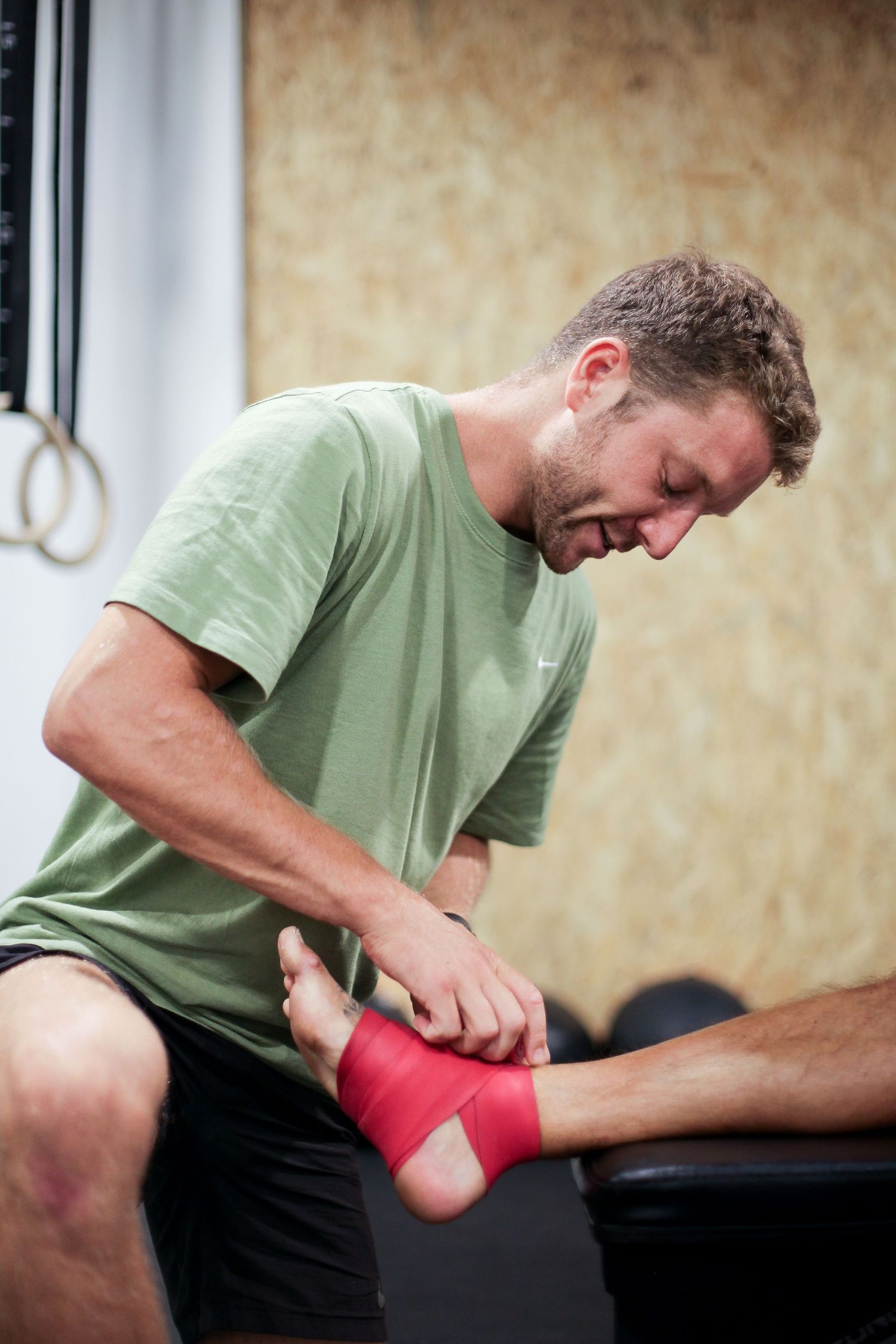 Physical therapist applying red therapeutic tape to patient's foot.