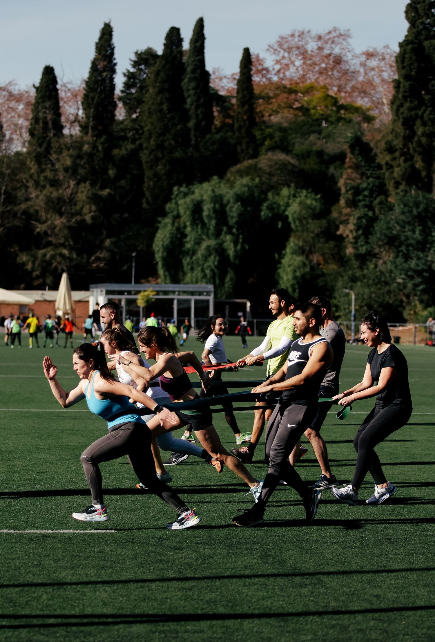 Group fitness class performing synchronized lunges on an outdoor field with cypress trees.