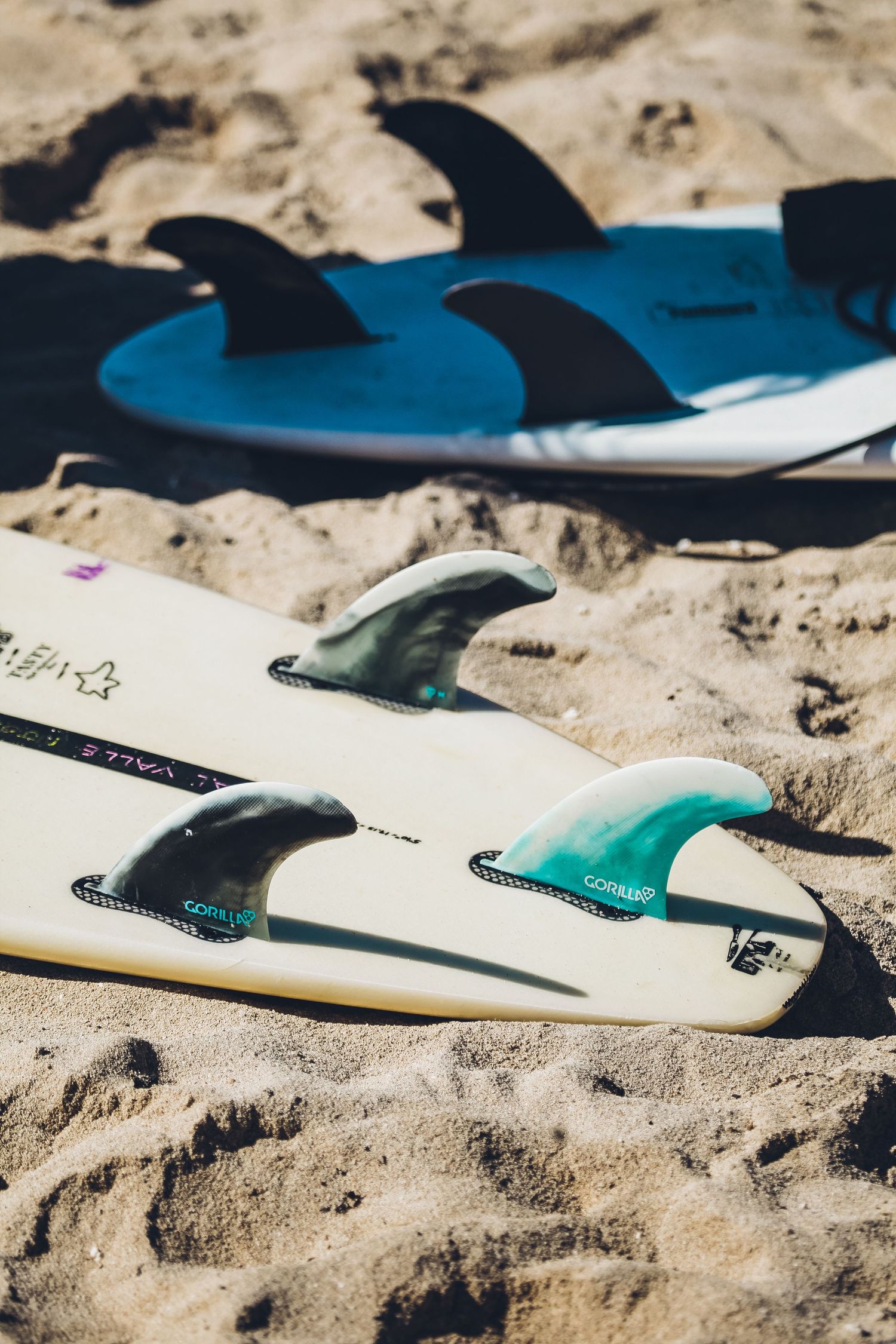Surfboards lined up on sandy beach in bright sunlight.