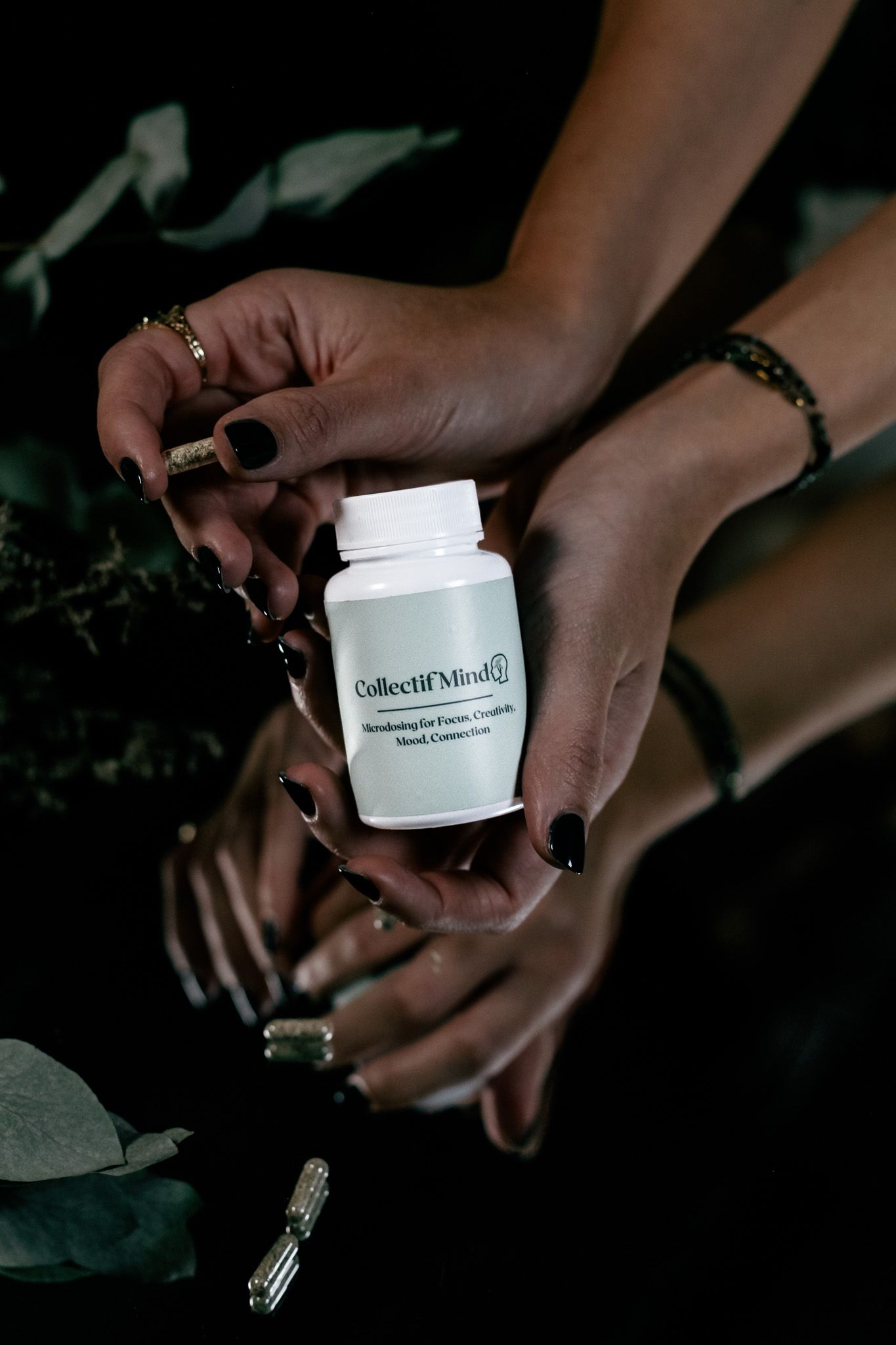 Hands with dark nail polish hold and open a white skincare product container in dim lighting.