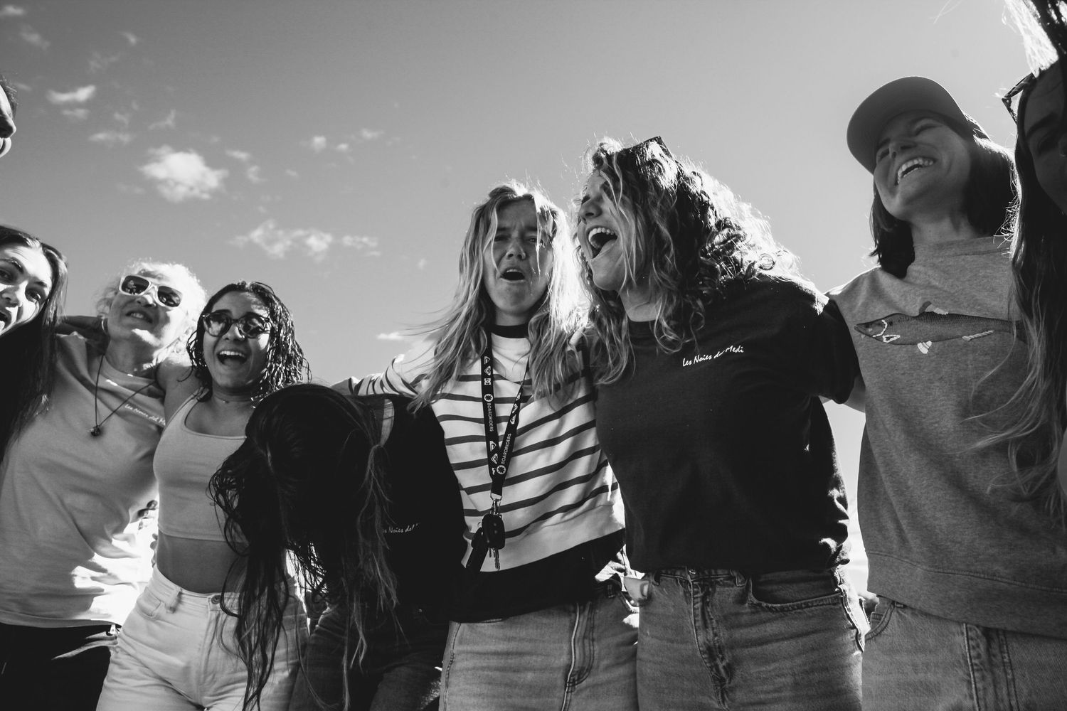 Black and white photo of friends gathered outdoors under cloudy sky.