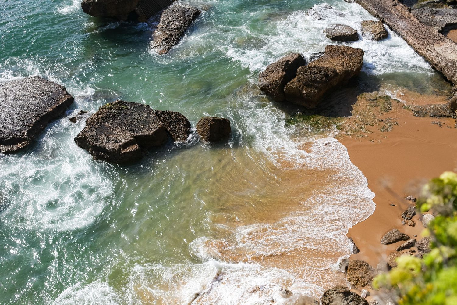 Turquoise ocean waves crashing against rocky coastal cliffs and sandy beach.
