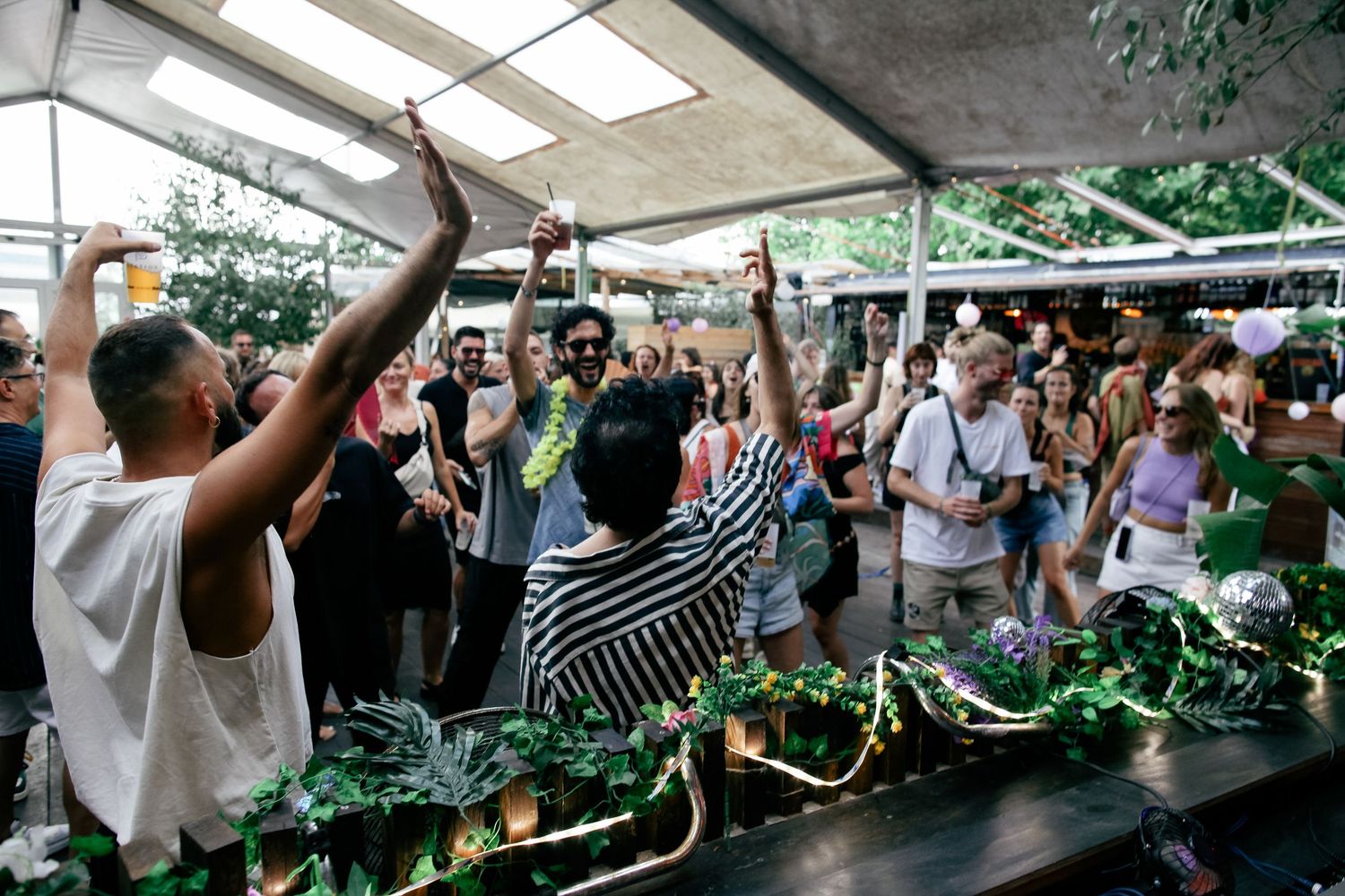 A crowded outdoor event space with white canopy and hanging greenery decorations.