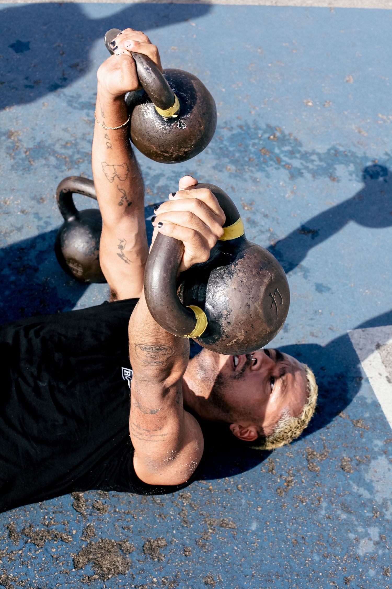 Athletic person lifting heavy kettlebells during outdoor workout on blue surface.