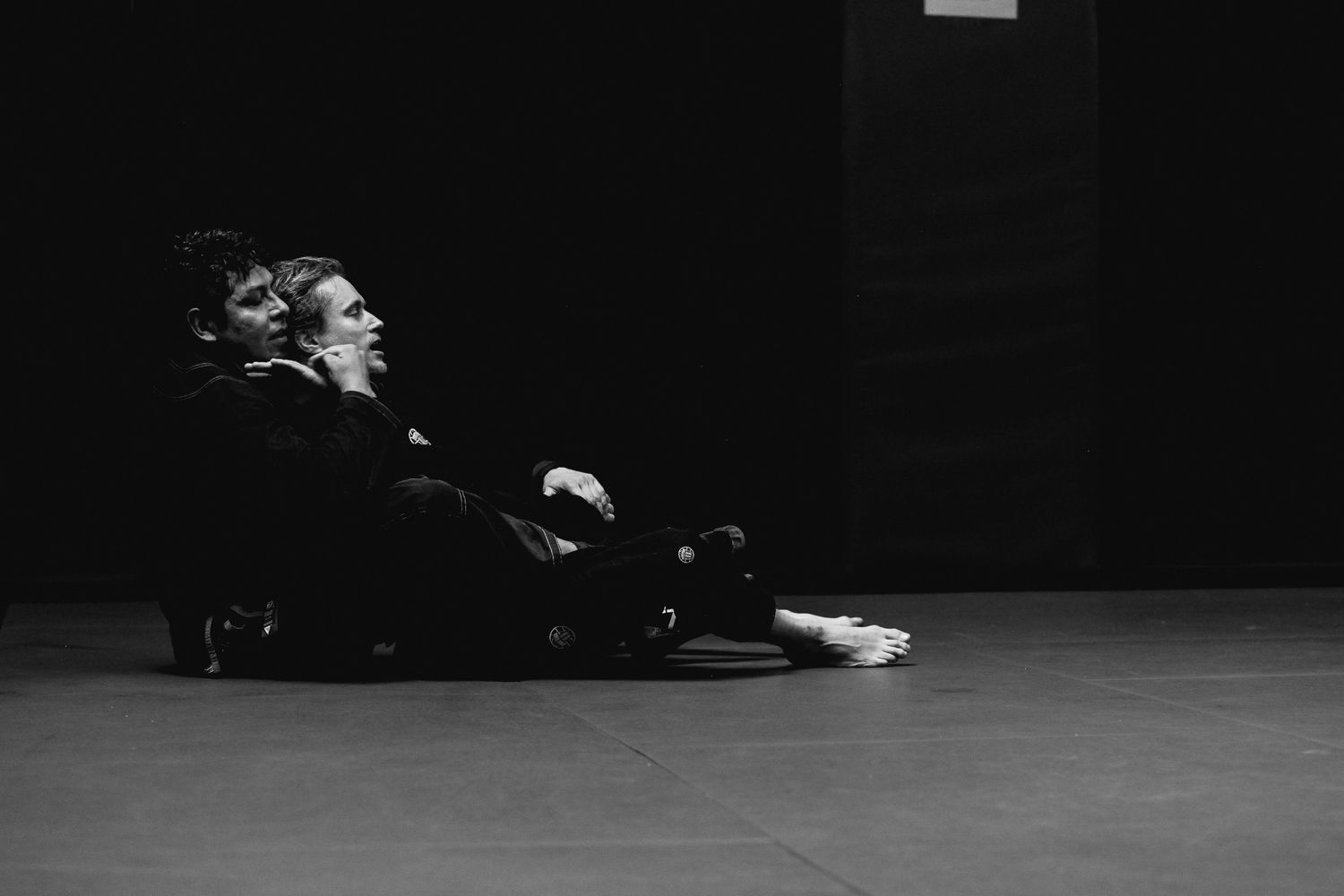Athletes practicing grappling techniques on a dark floor during martial arts training.