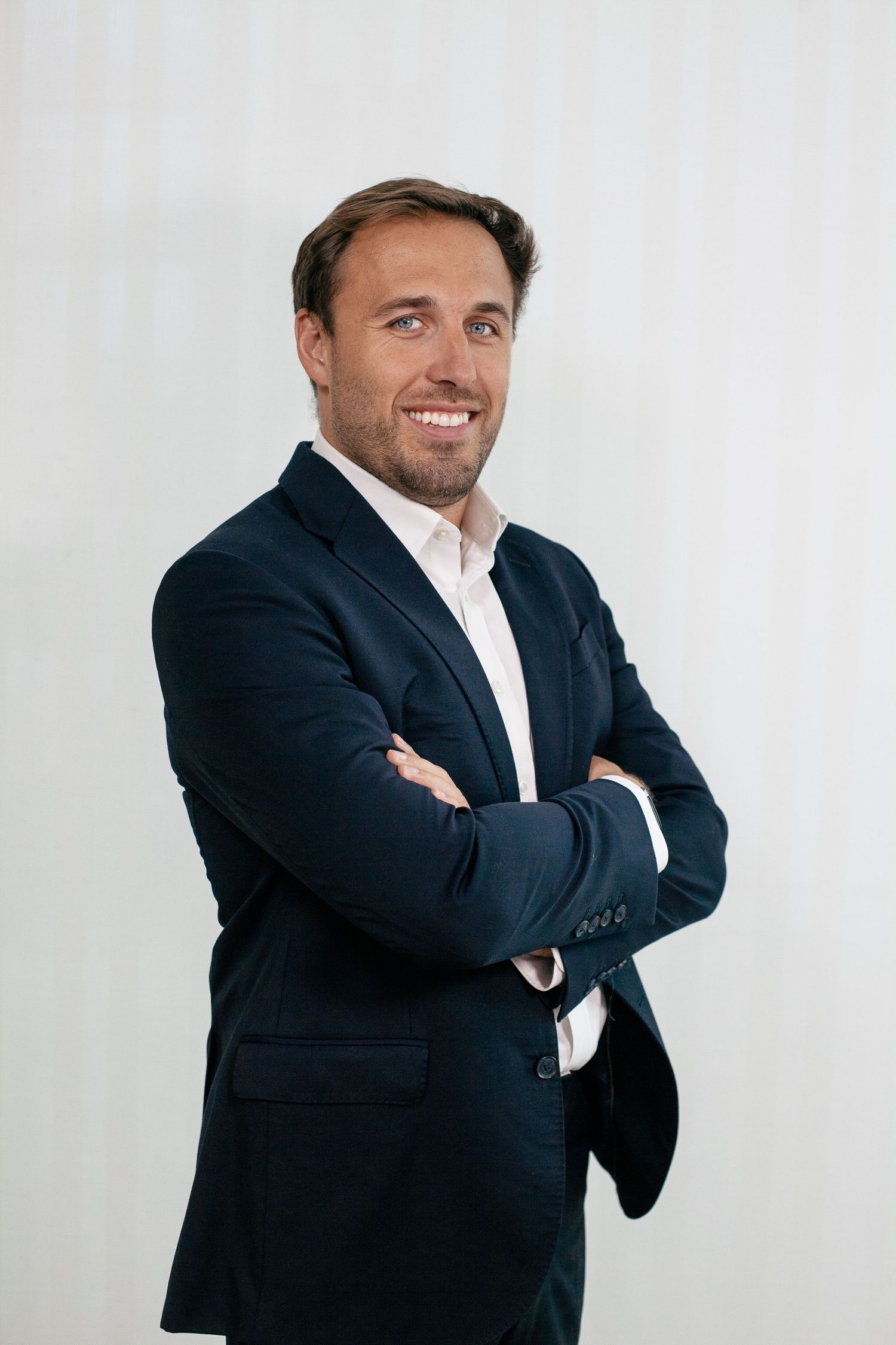 Business professional in navy suit poses confidently against white background.