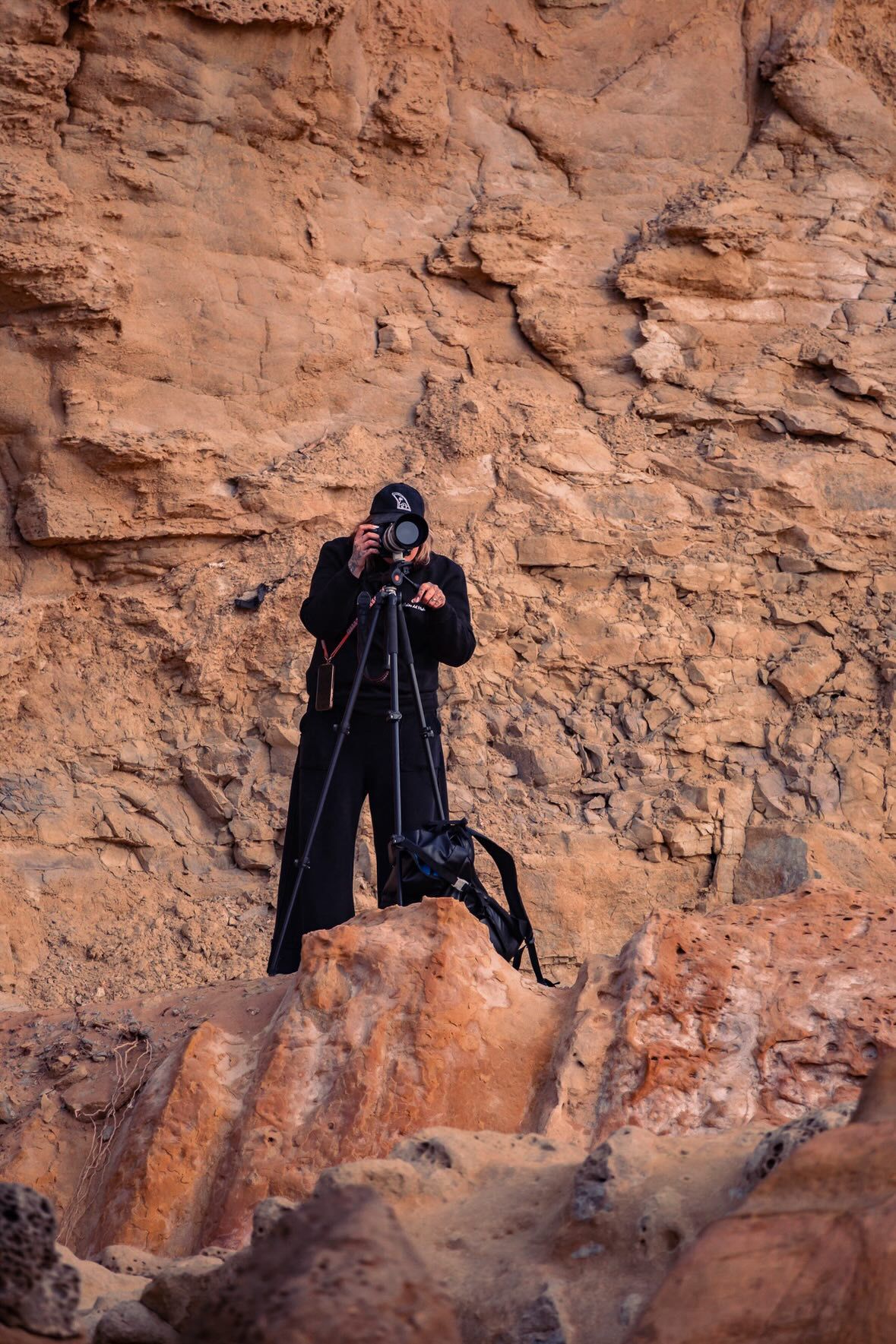 Photographer in black clothing captures shots against a red rock cliff face in a sequence of images.