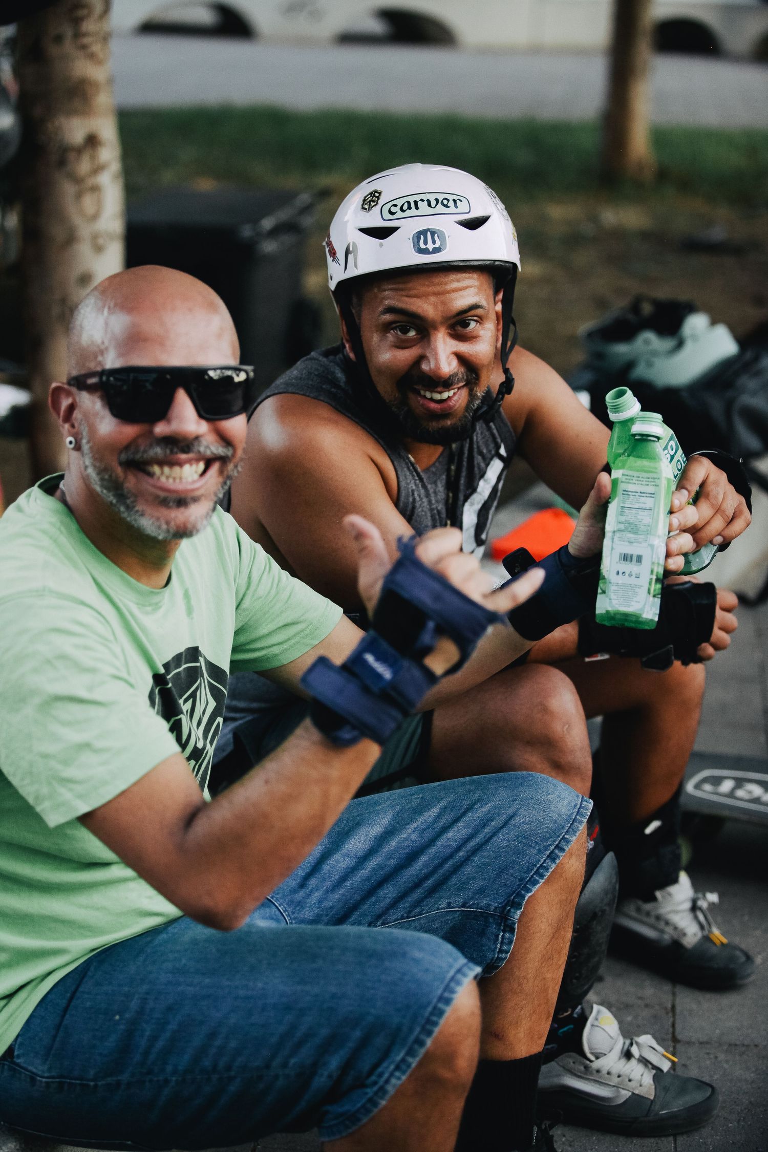 Two athletes taking a break during outdoor activities while holding water bottles and wearing protective gear.