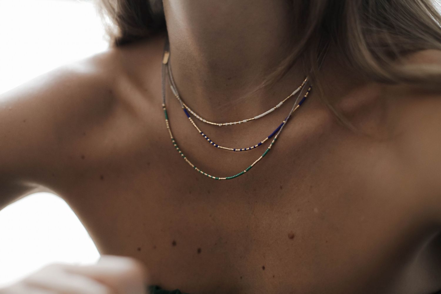 Close-up of layered silver chain necklaces against bare shoulders in soft lighting.