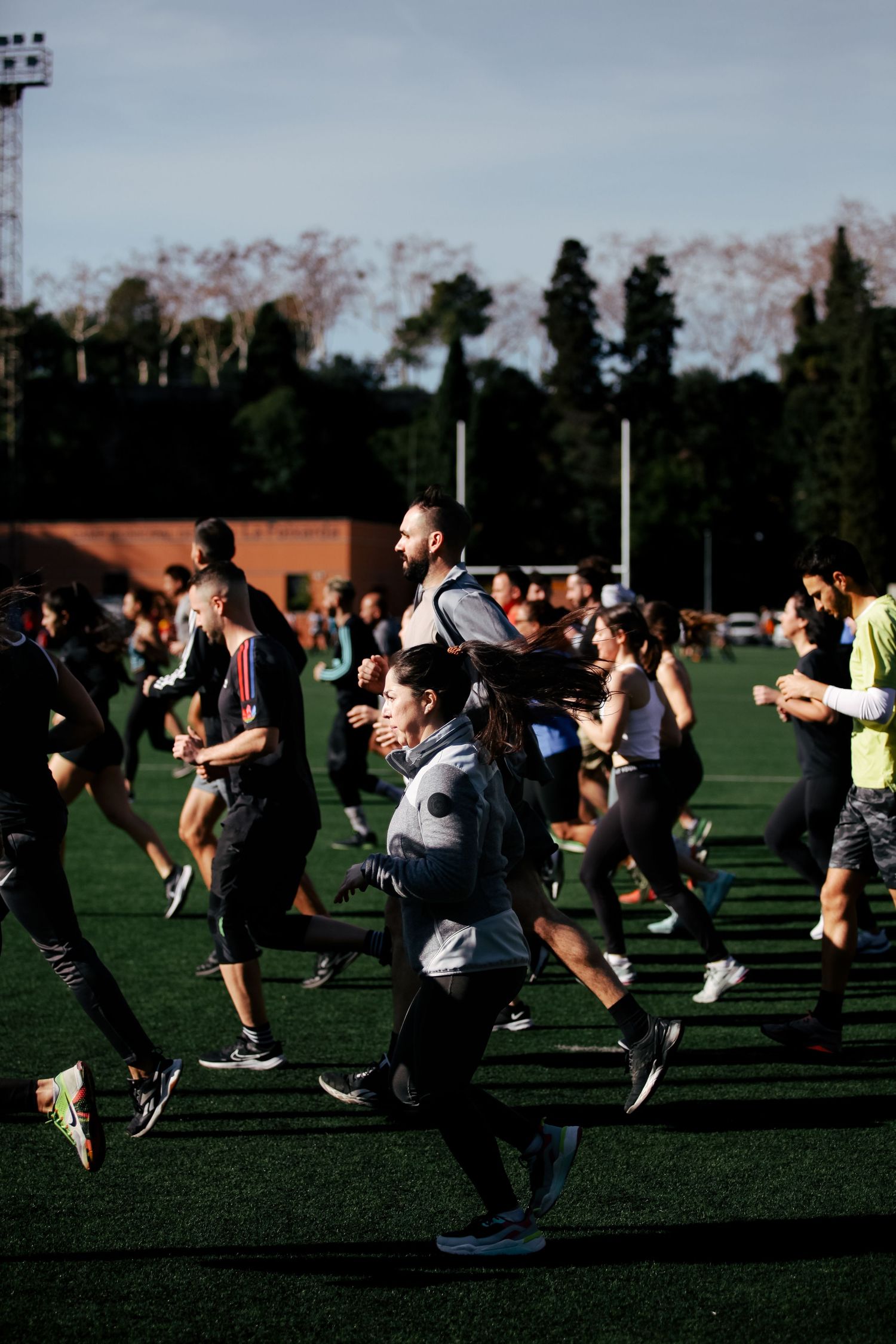 Large group of athletes running together on an outdoor sports field at dusk.
