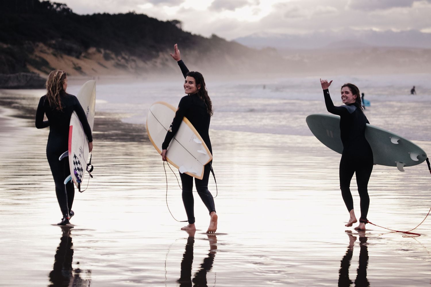 Silhouettes of surfers walking along misty beach at sunset.
