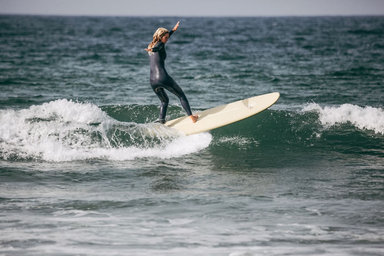 A surfer riding a longboard on a gentle ocean wave.