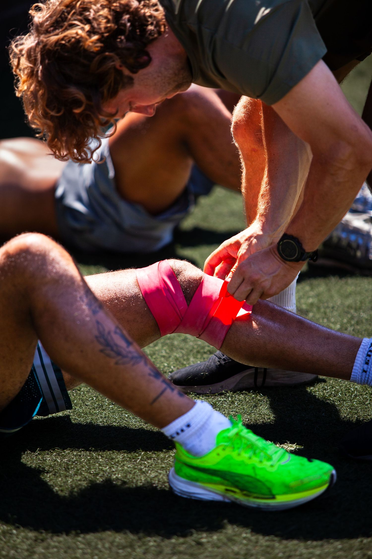 Athletic trainer applying therapeutic tape to athlete's foot on sports field.