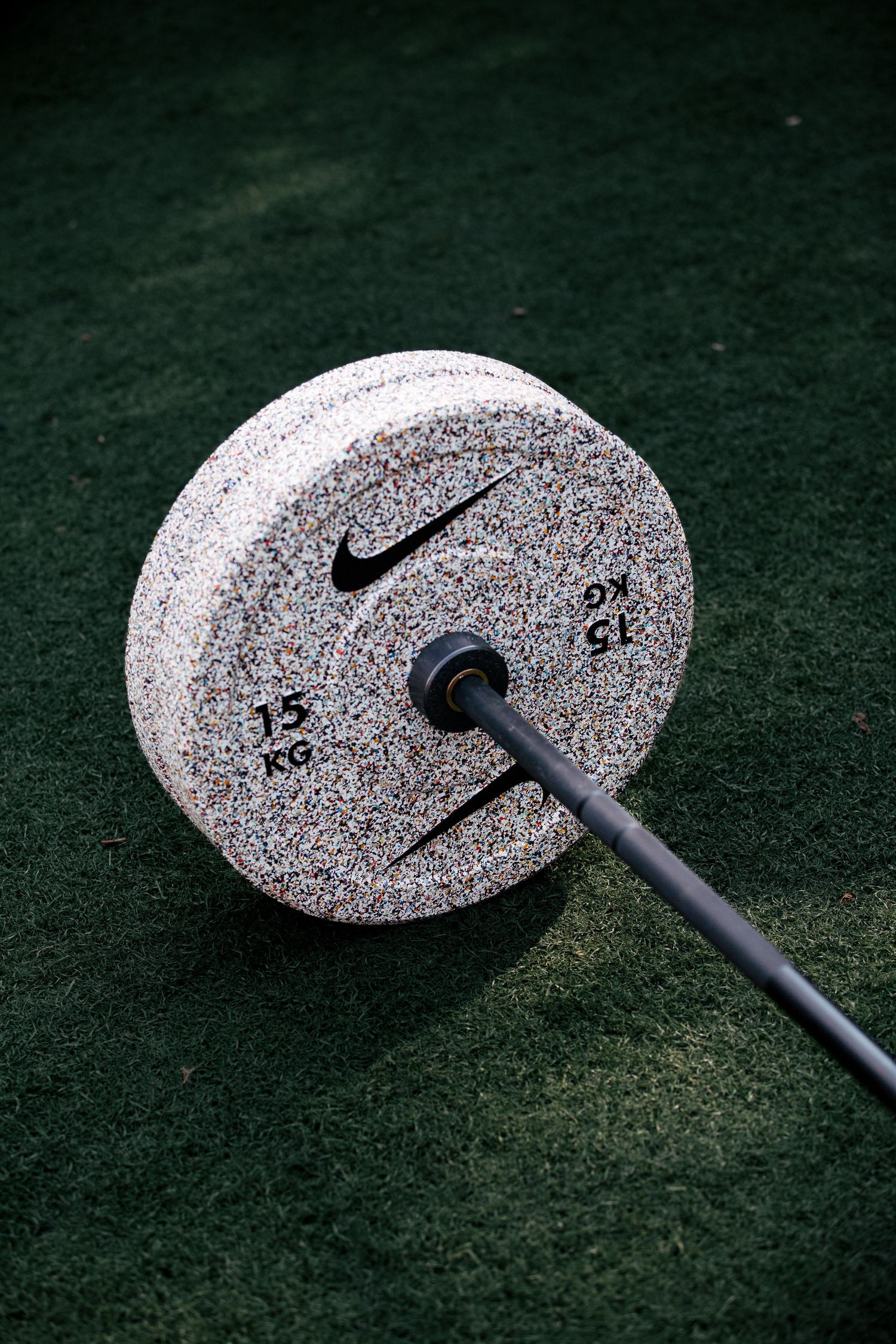 Close-up shots of speckled weight plates on artificial turf with black metal bar.