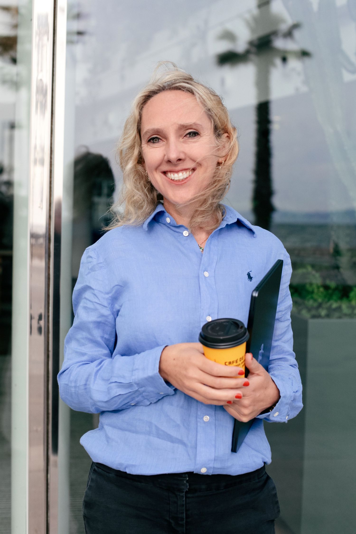 Professional in light blue button-down shirt holding yellow travel mug outdoors.