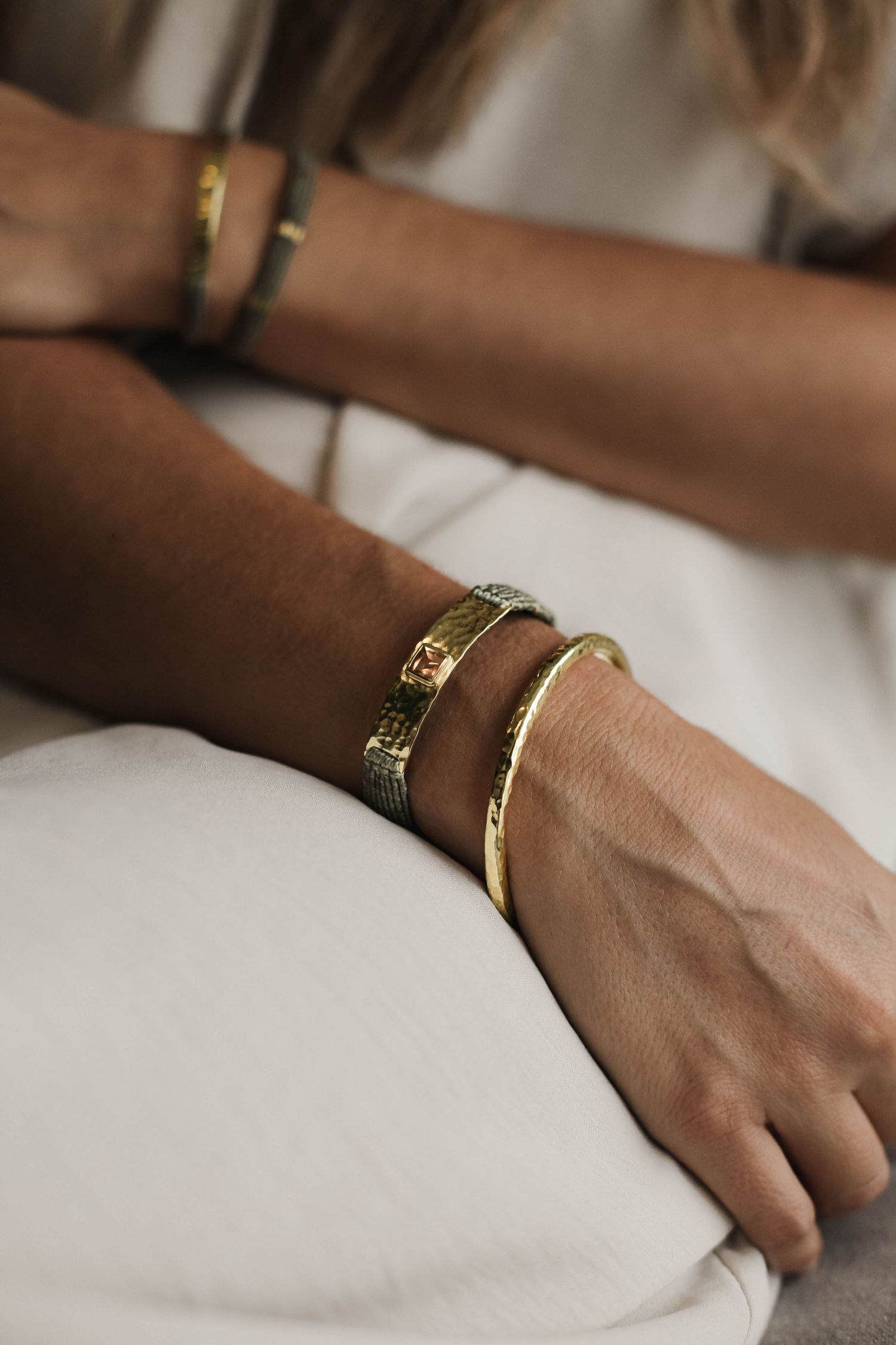 Hand wearing delicate gold rings against white bedding in soft natural light.
