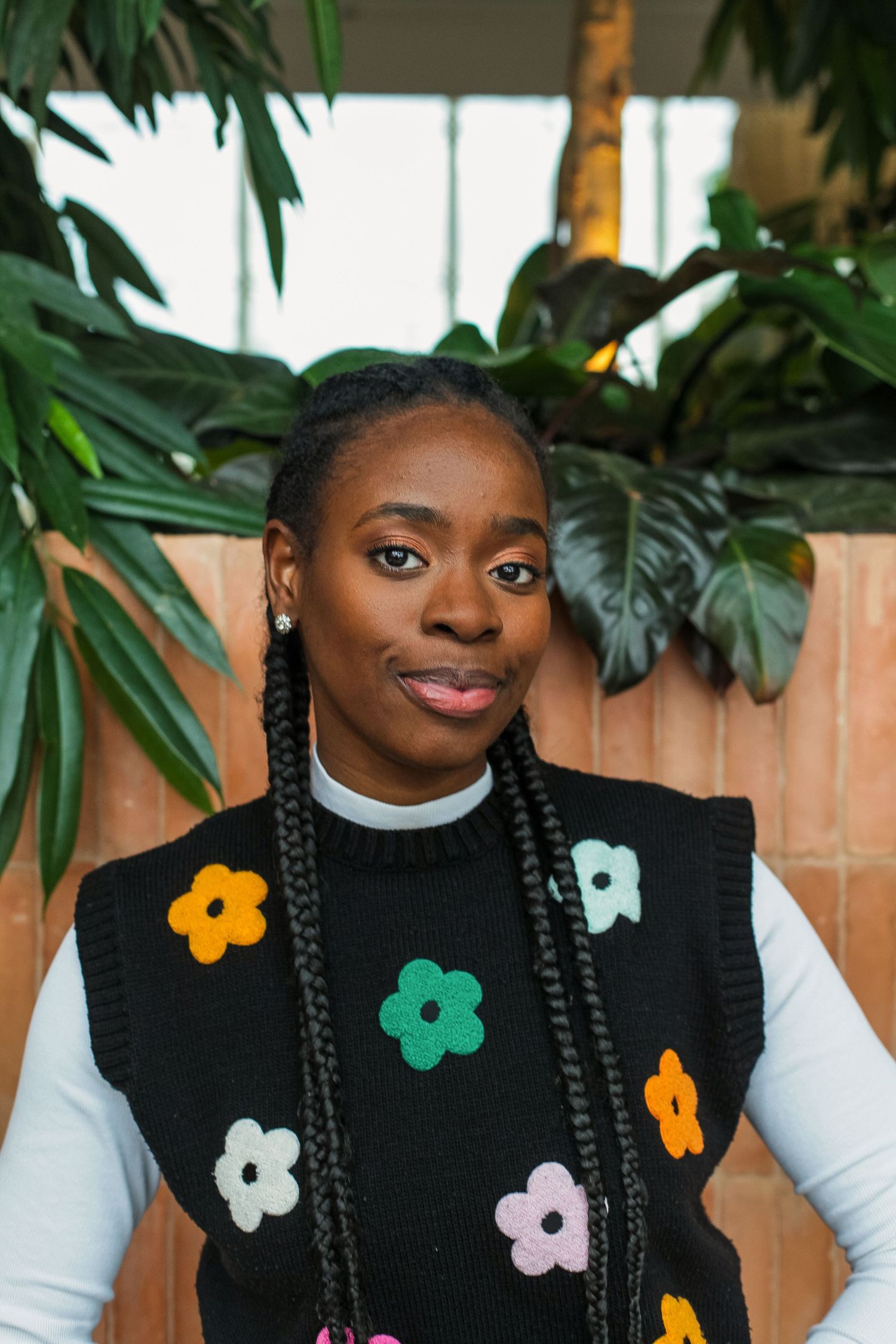 Playful black sweater decorated with colorful flower appliques against foliage background.