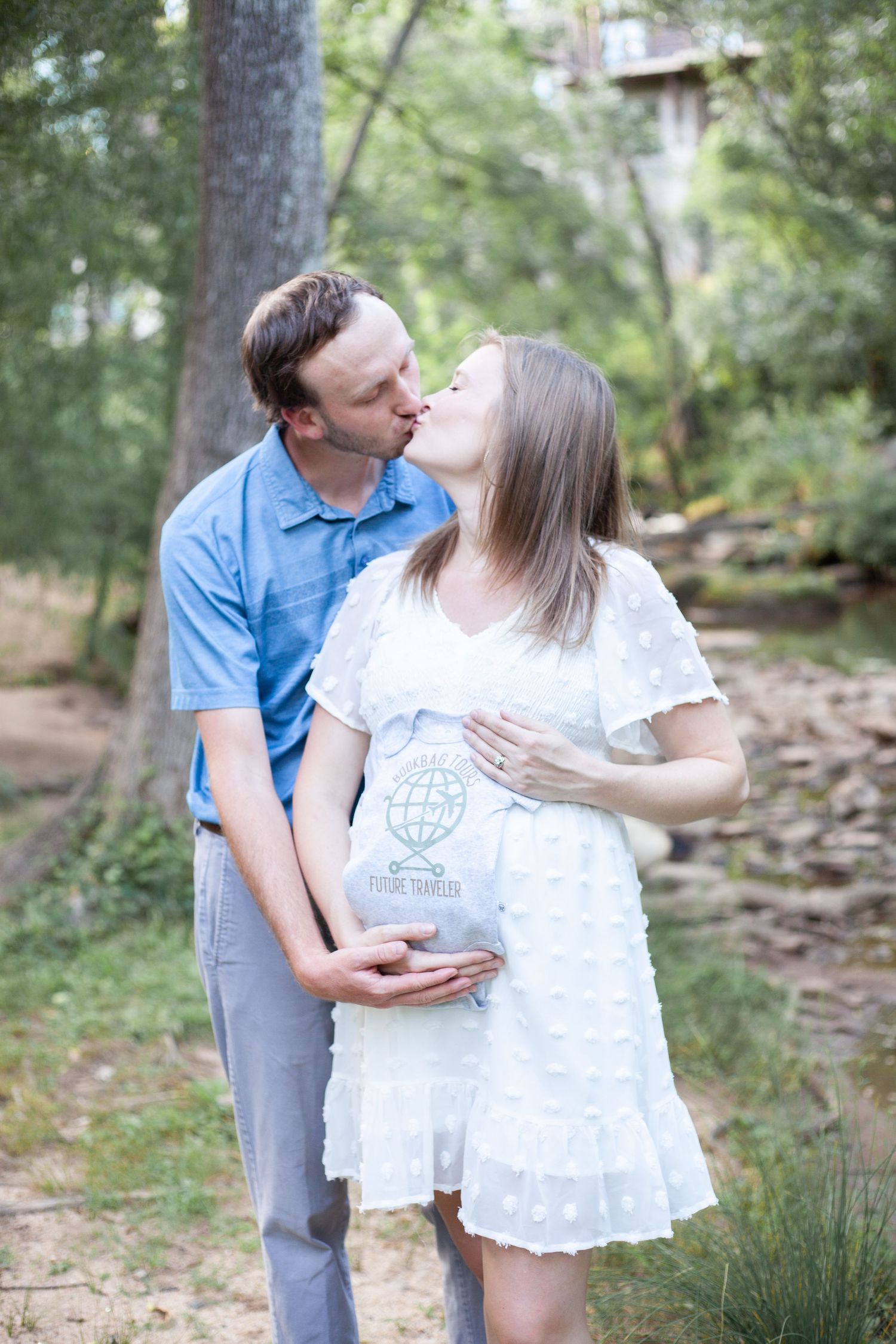 Maternity photography in falls park Greenville for new parents to be, holding up a cute onsie for their new baby
