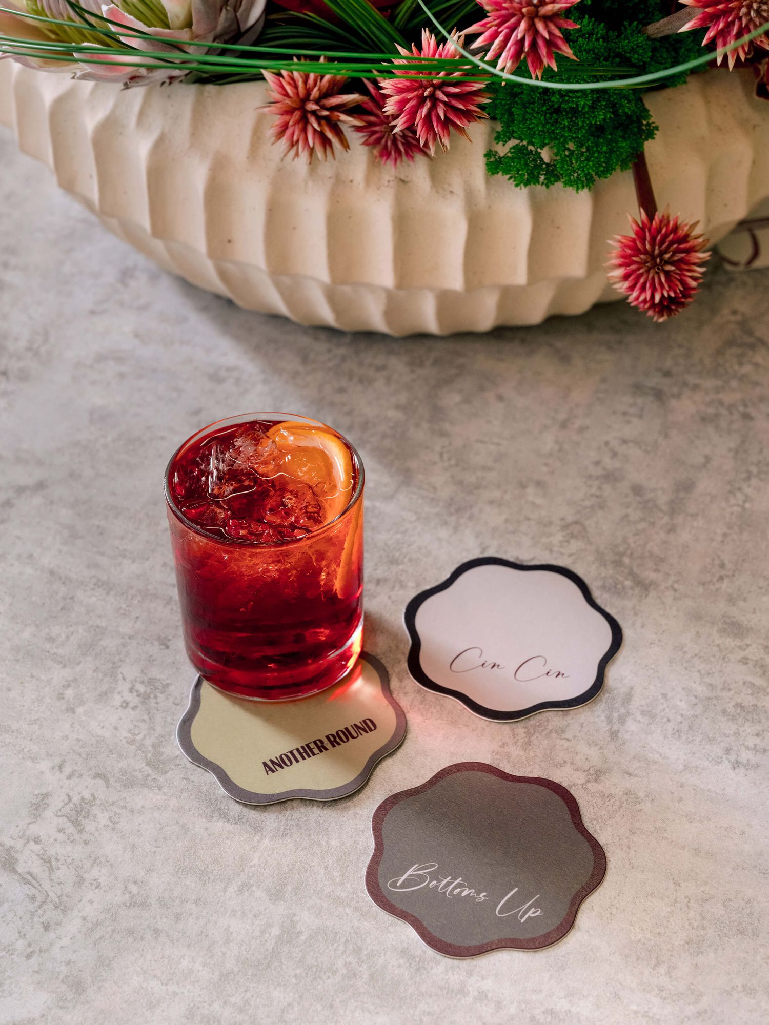 Red cocktails with floral garnishes served on elegant stone coasters at an upscale event.