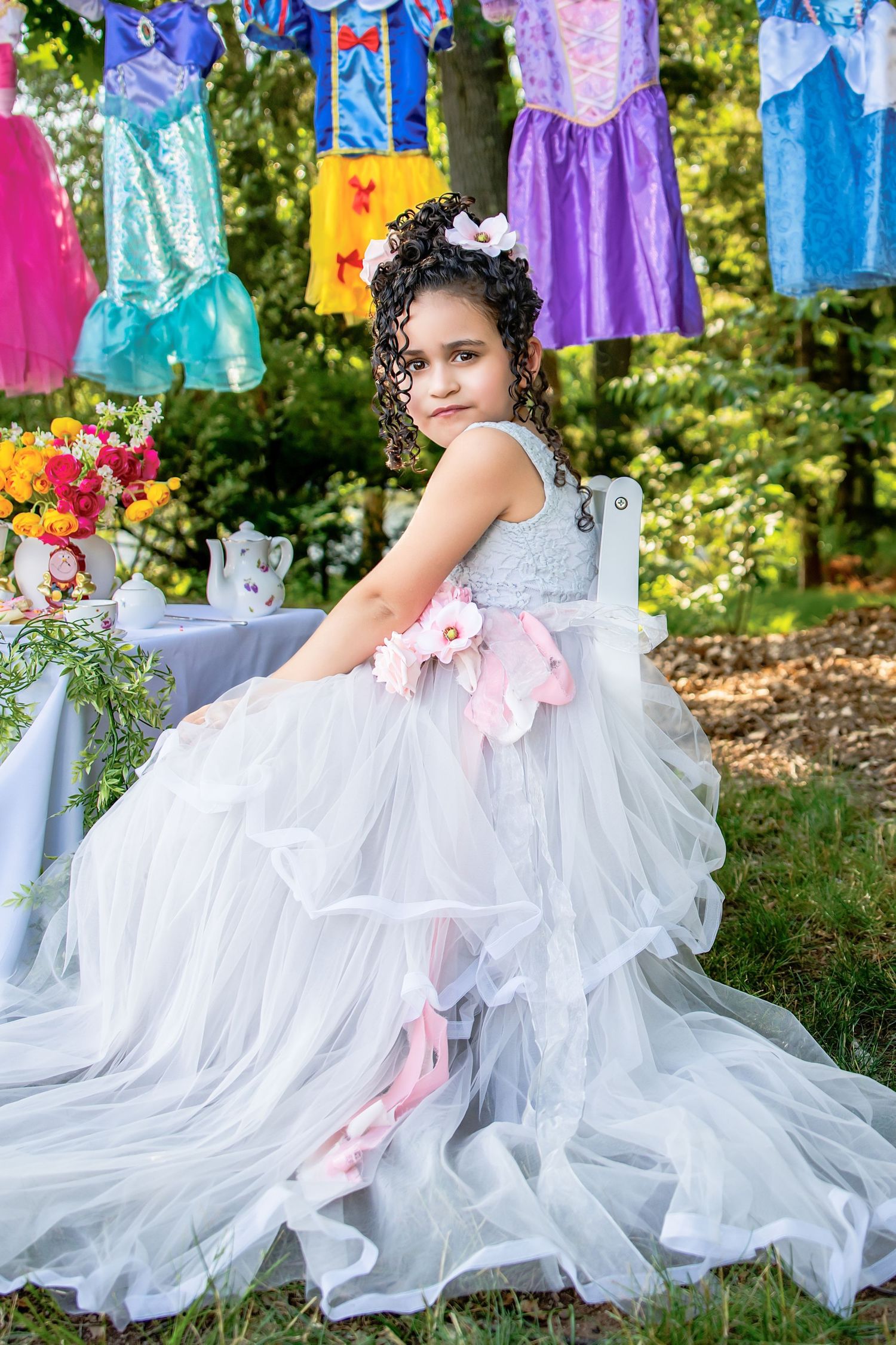 Young girl in a white tulle princess gown with pink flowers at an outdoor princess-themed party.