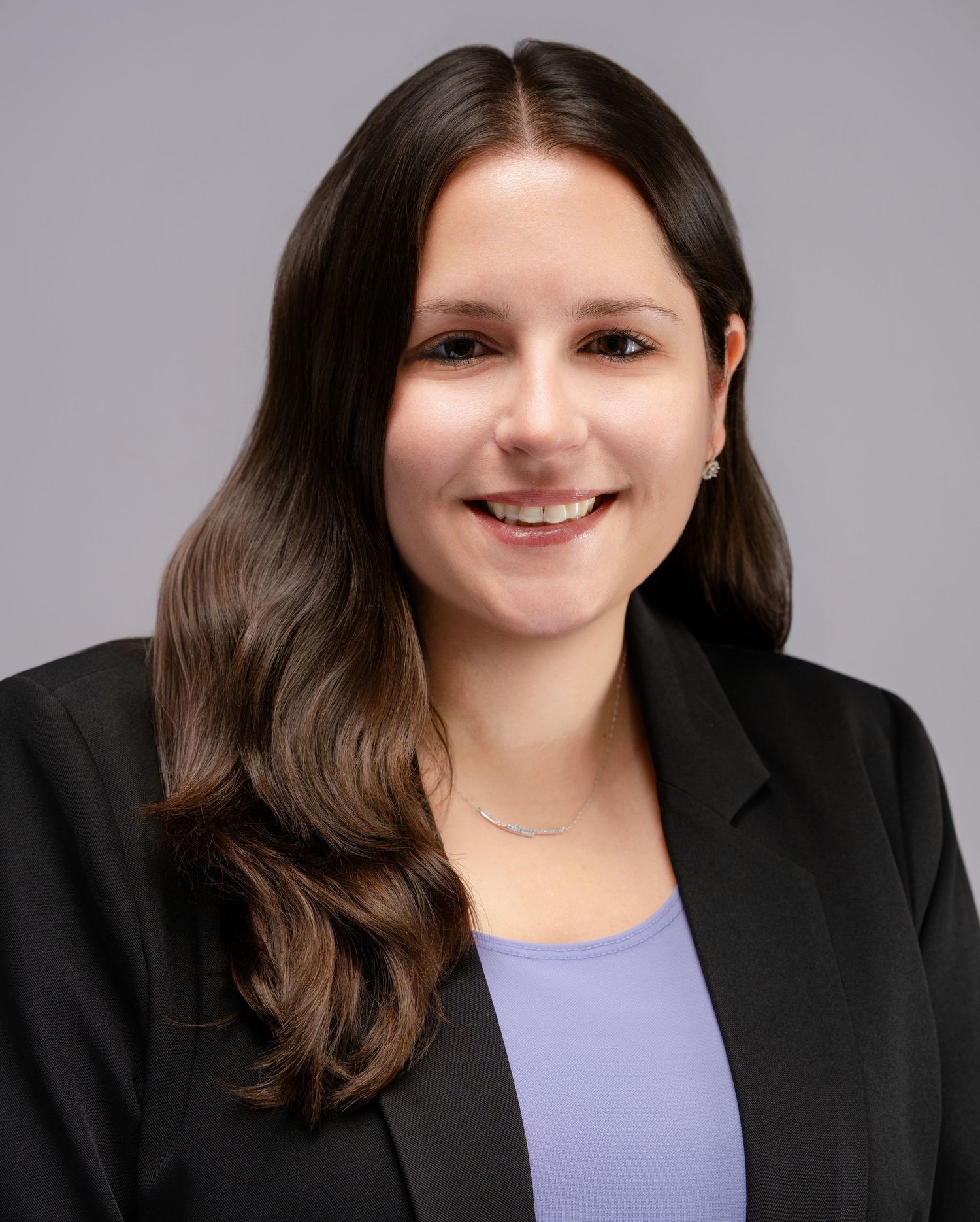 Professional headshot of a brunette woman in black blazer and lavender top.