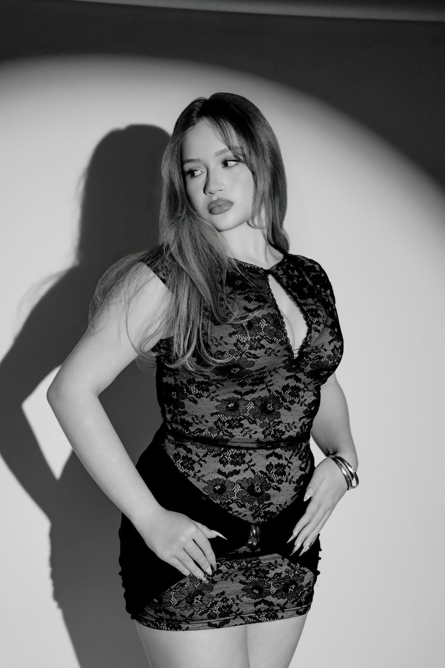 Black and white portrait of woman in black lace mini dress posing confidently under spotlight.