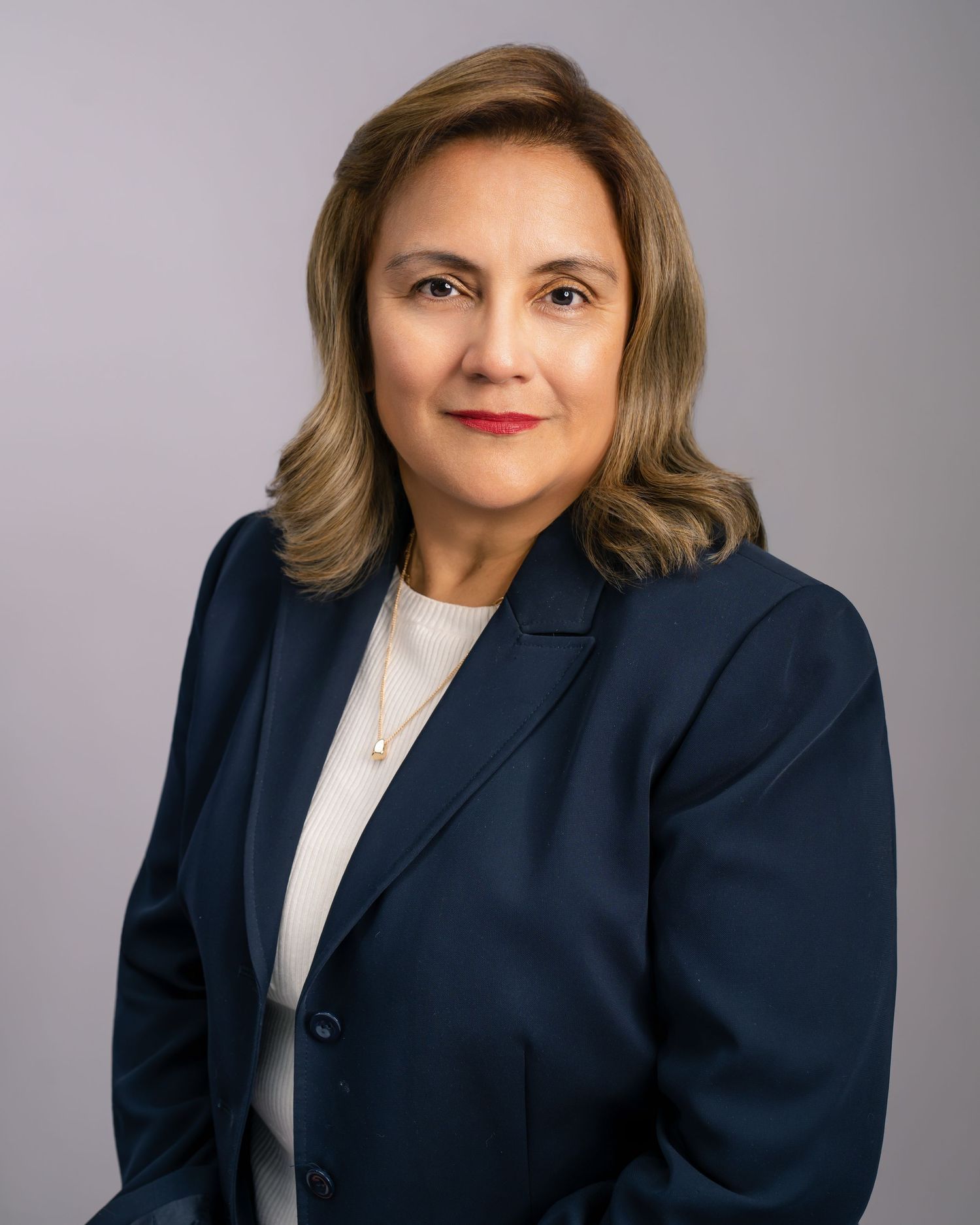 Professional headshot of a woman in navy blazer with gold necklace.