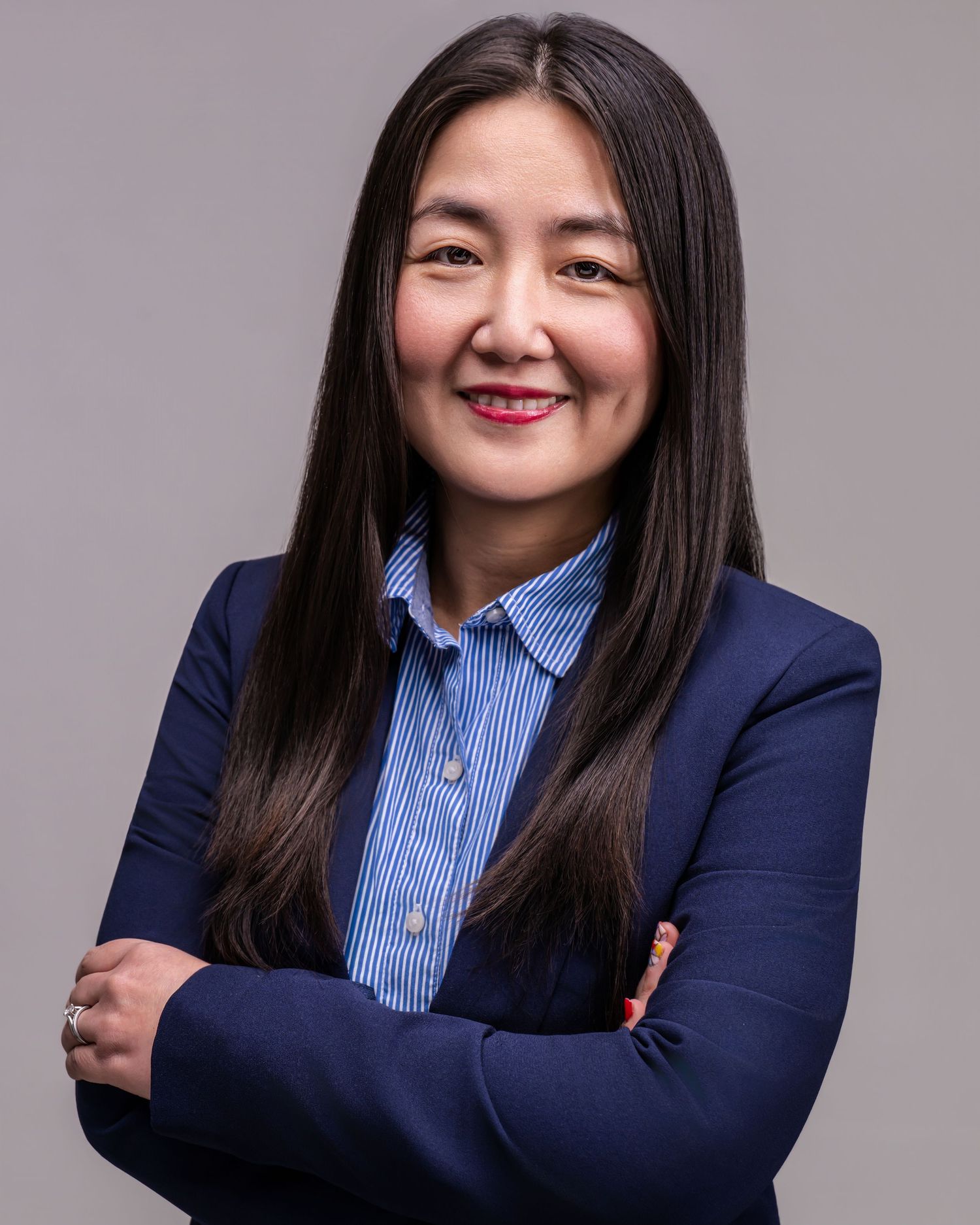 Asian woman in navy blazer with arms crossed, professional business headshot.