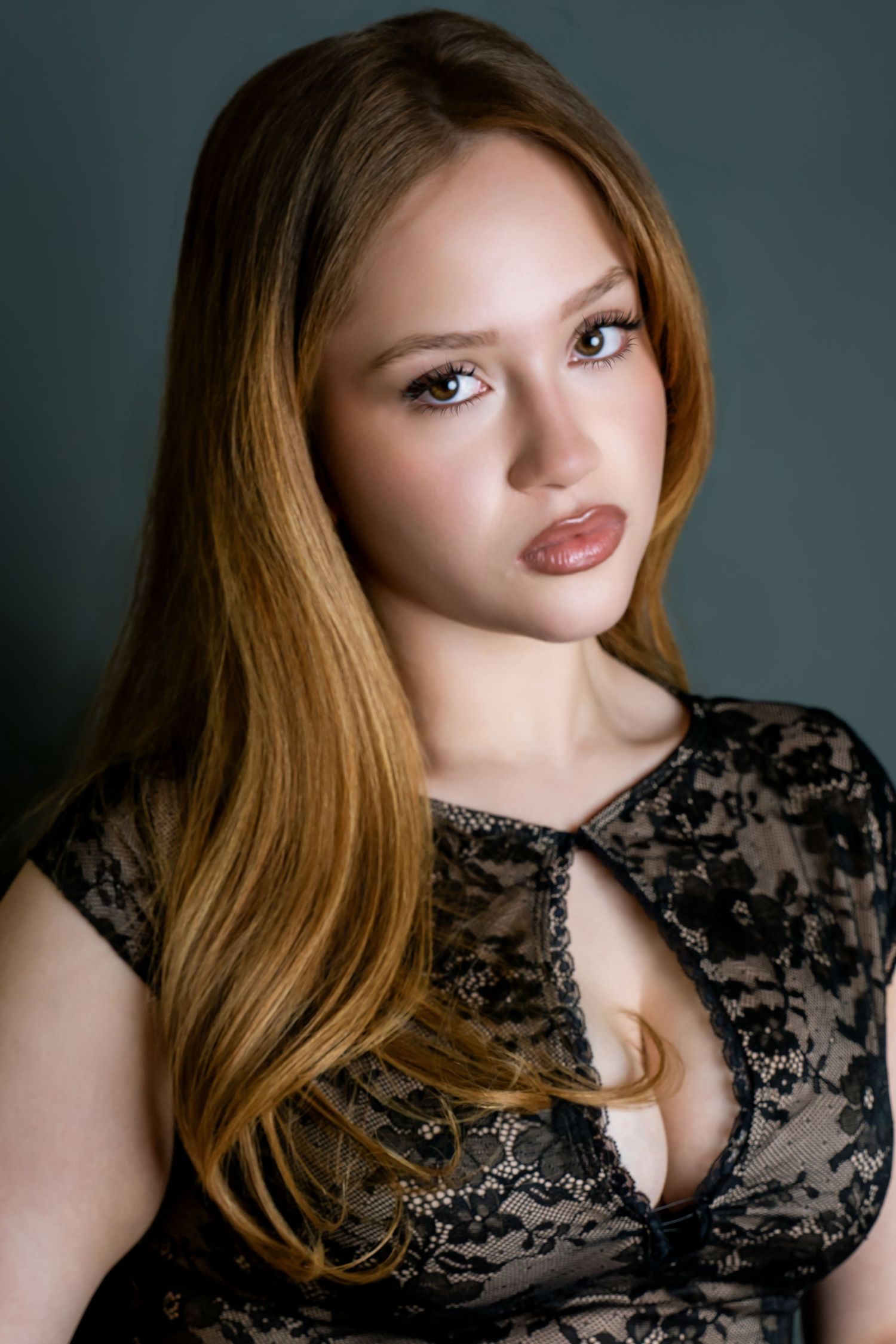 Close-up portrait of young woman with long auburn hair in black lace dress on dark background.