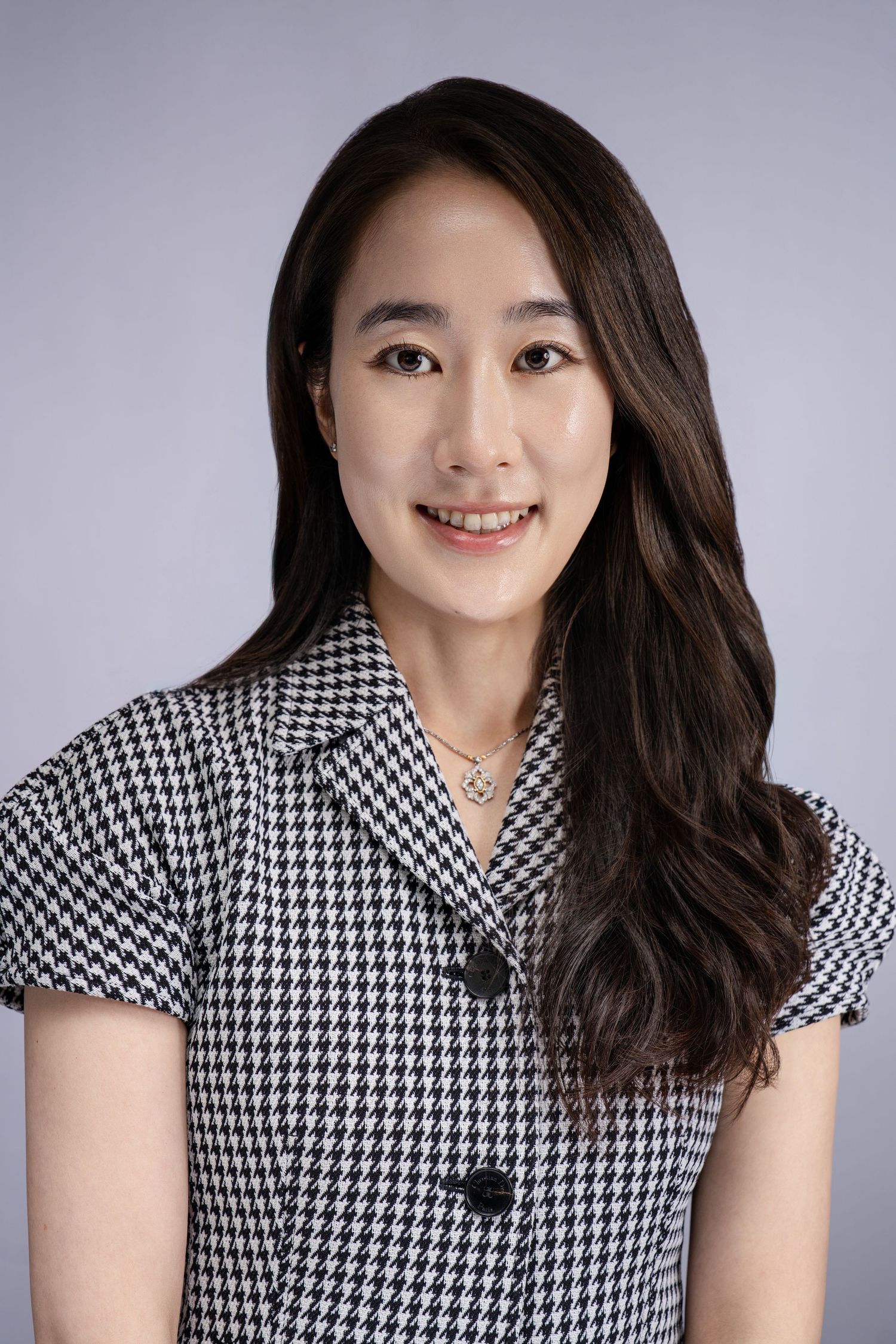 Young Asian woman smiling in houndstooth blazer, professional studio portrait.