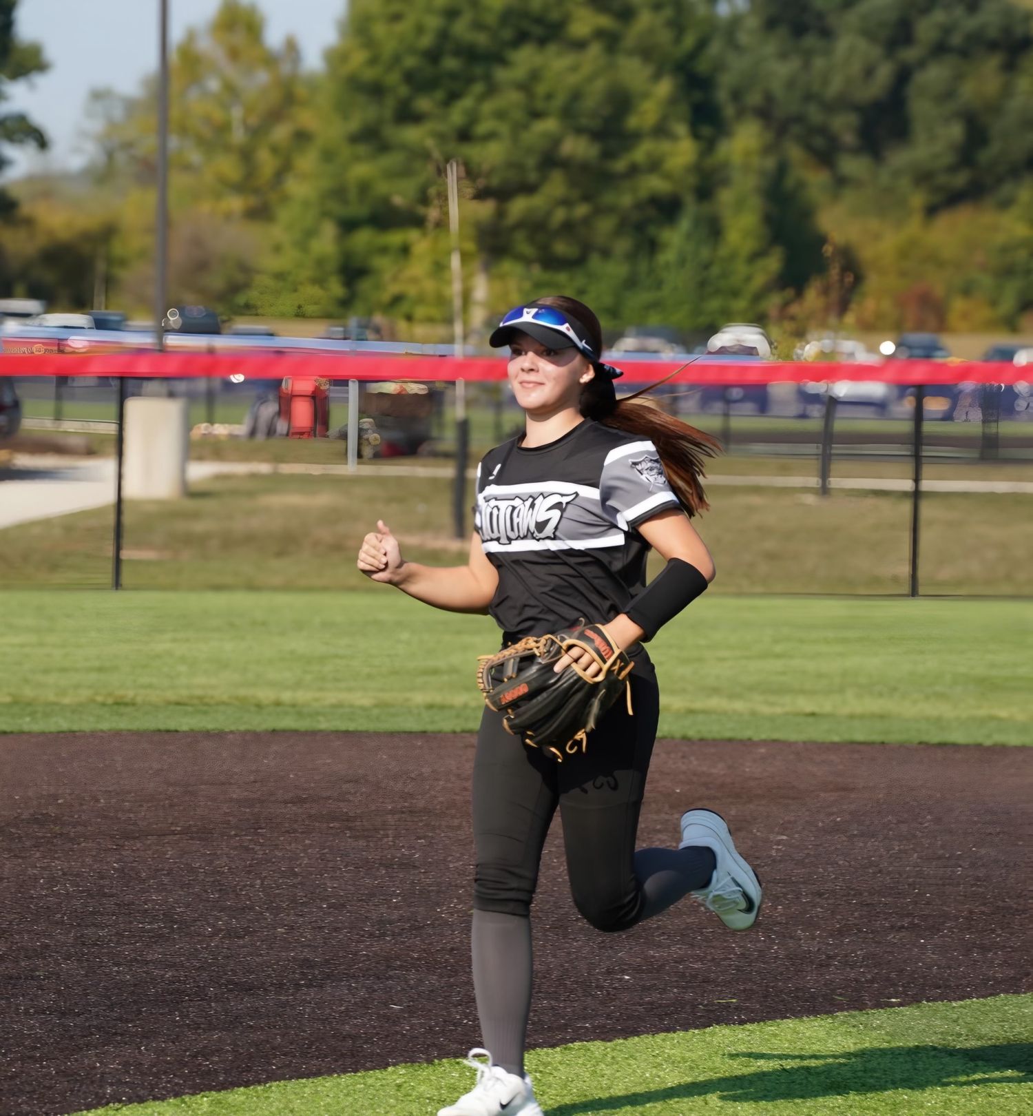 A softball pitcher in black uniform demonstrates pitching form during practice on a dirt field.