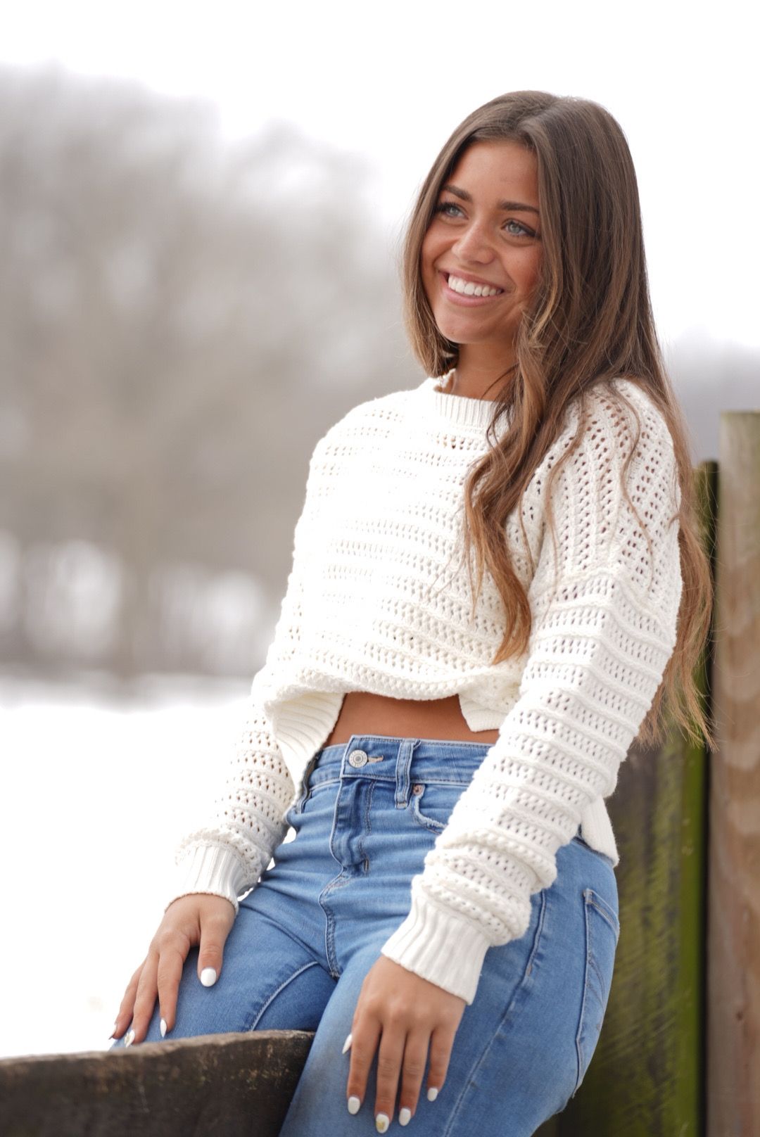 Person in a cozy white knit sweater and blue jeans sits casually outdoors during winter.