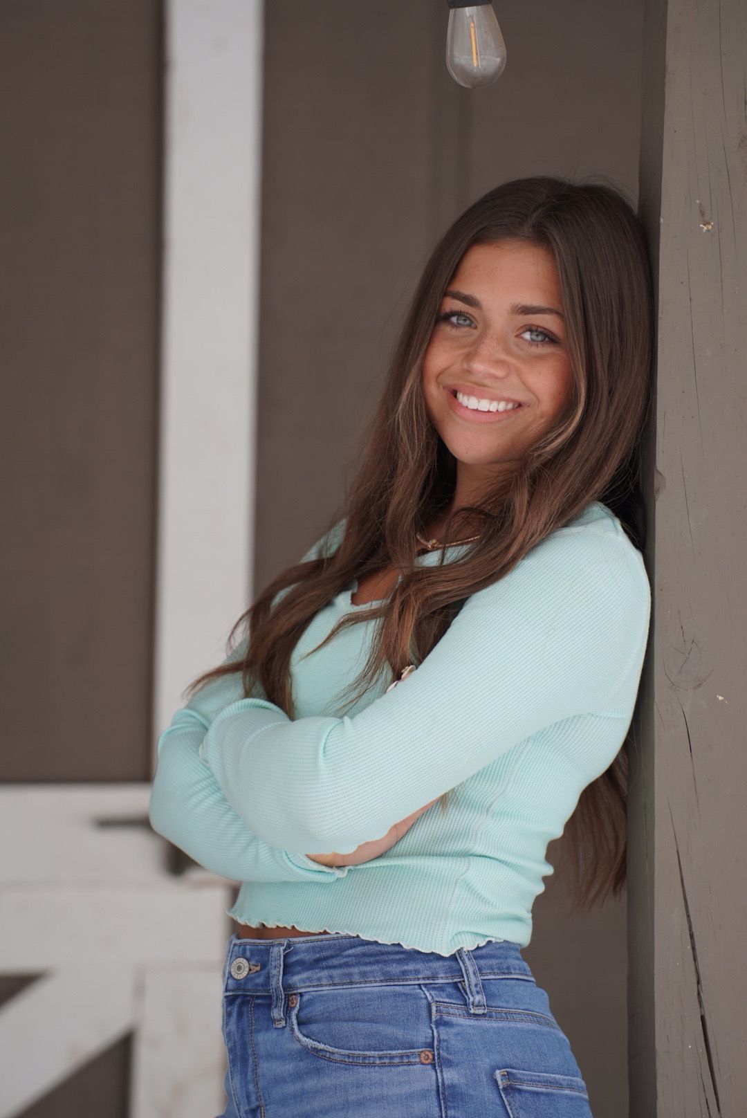 Casual portrait showing bright smile and relaxed pose wearing mint sweater and jeans while leaning against wall.