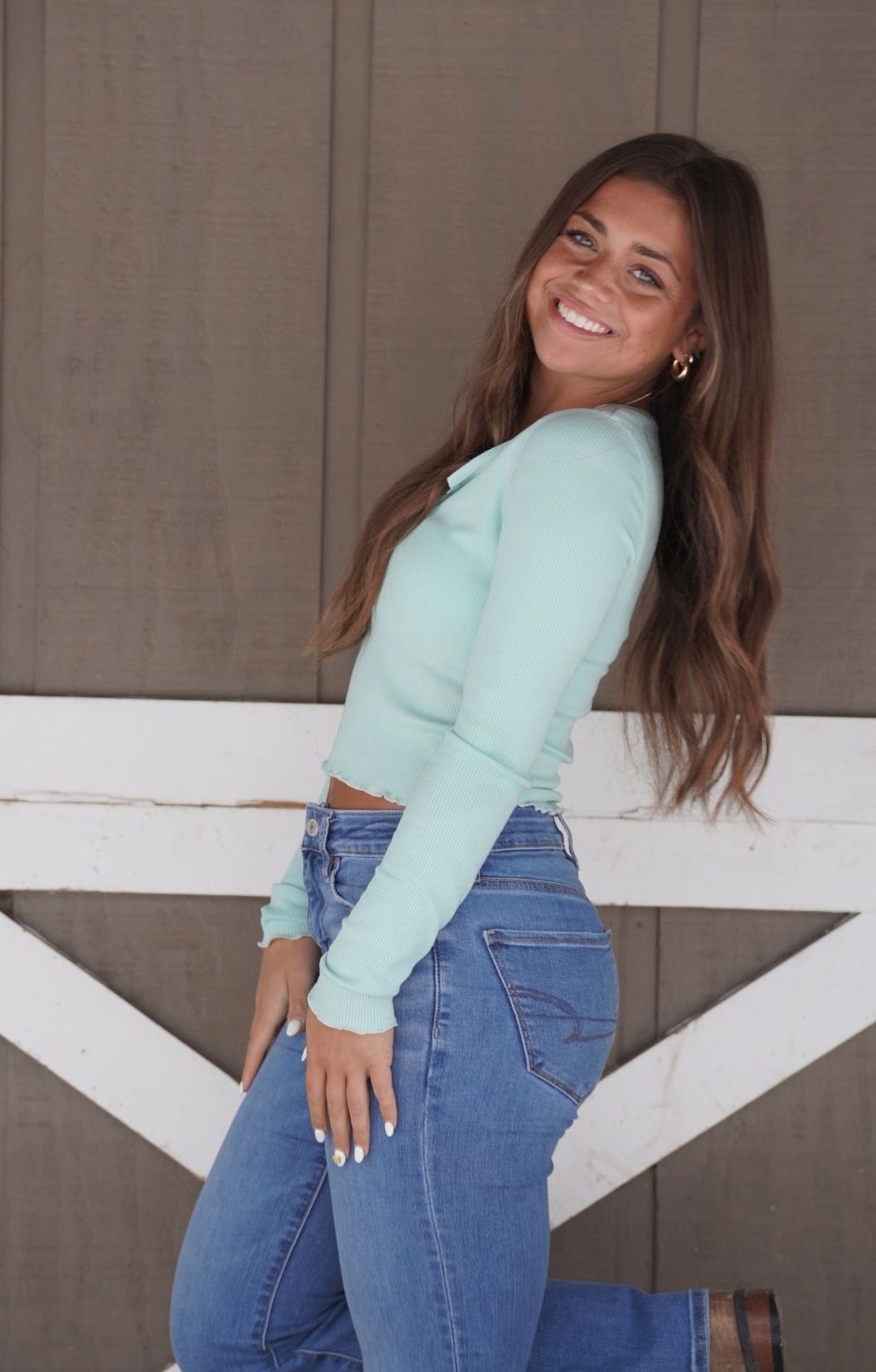 Woman in mint green sweater and high-waisted jeans poses playfully against a gray wall in multiple shots.