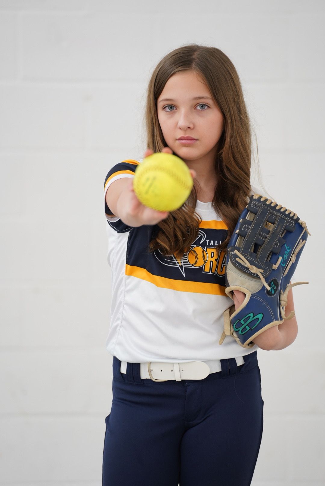 Softball player in navy pants and white top demonstrates catching positions with yellow ball and blue glove.